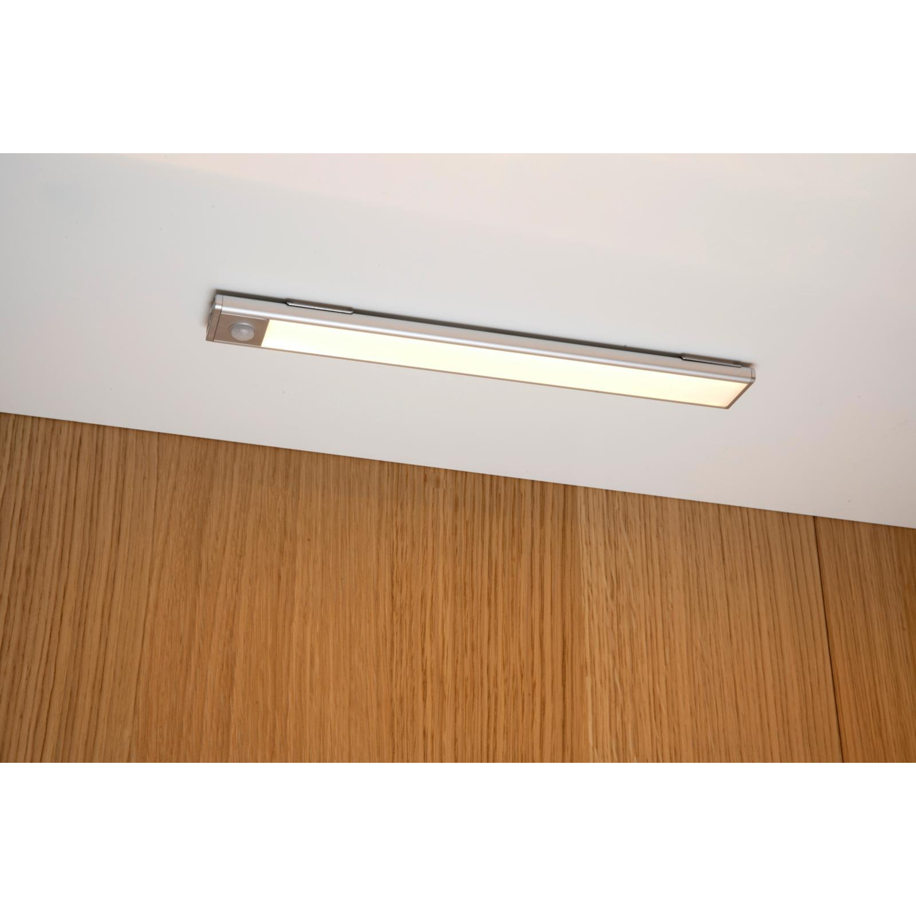 A rectangular LED light fixture on a white ceiling. Wooden paneling is below. The light is on.