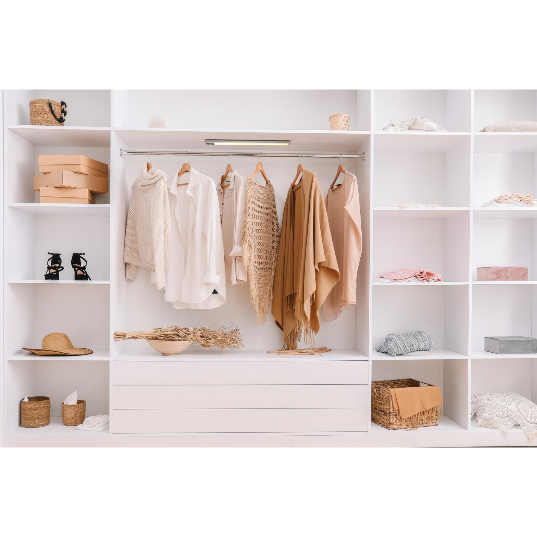 White closet with clothes, shelves with boxes, hats, and shoes. Neutral colors. Organized and clean.