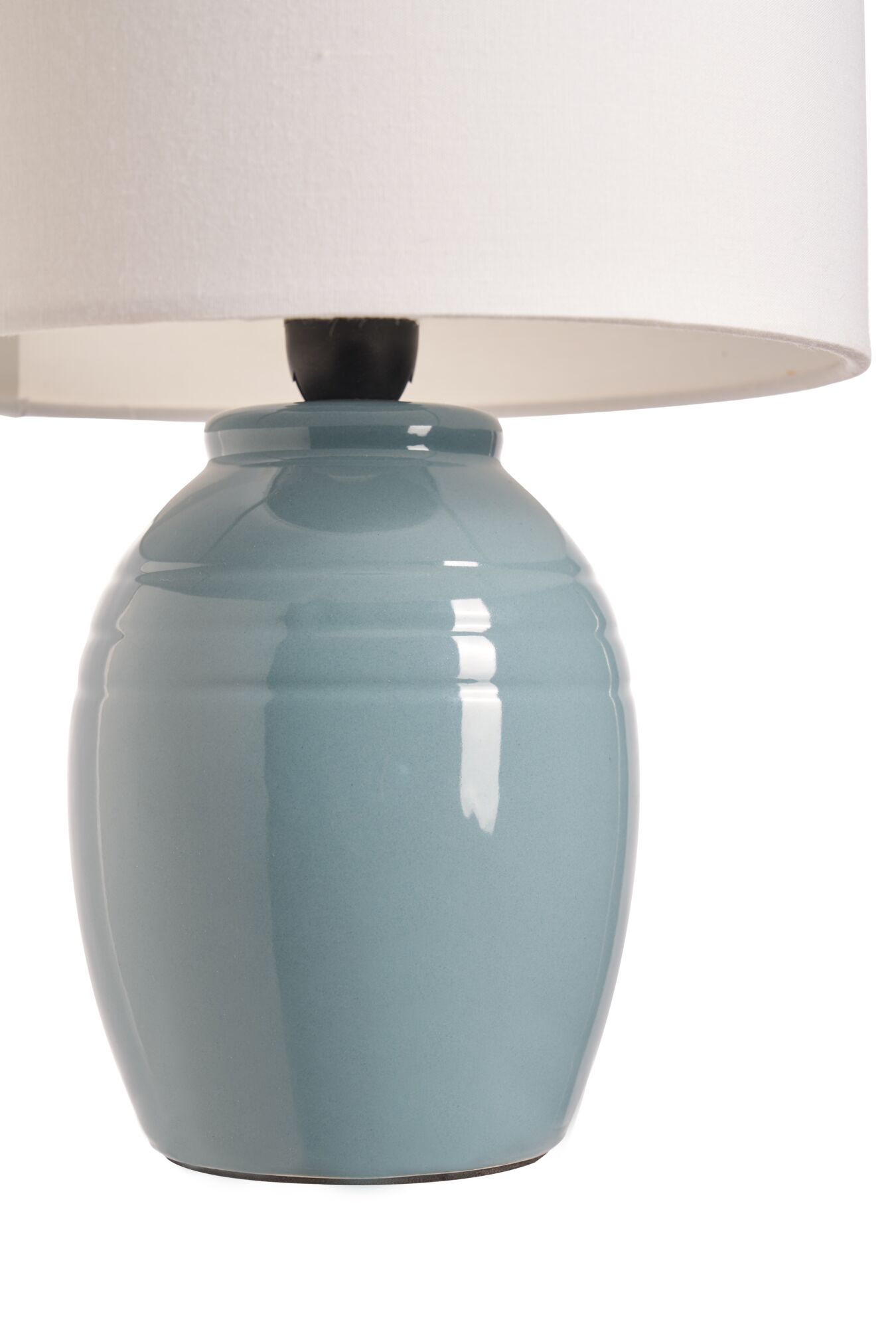 Niebieska ceramiczna podstawa lampy zwieńczona jest białym abażurem. Lampa znajduje się na białym tle.