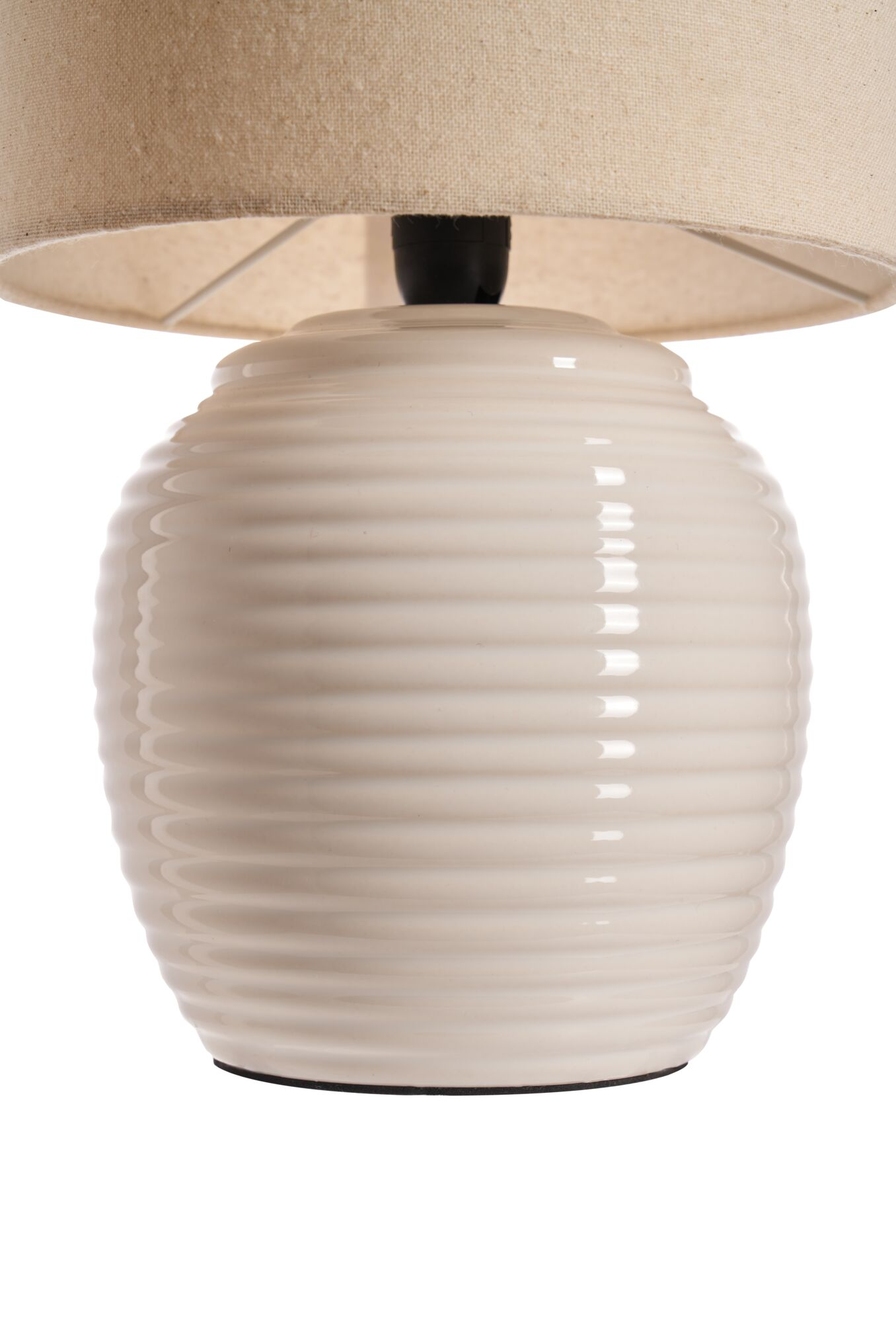 Kremowa lampa. Podstawa jest żebrowana, z beżowym abażurem. Tło jest białe.