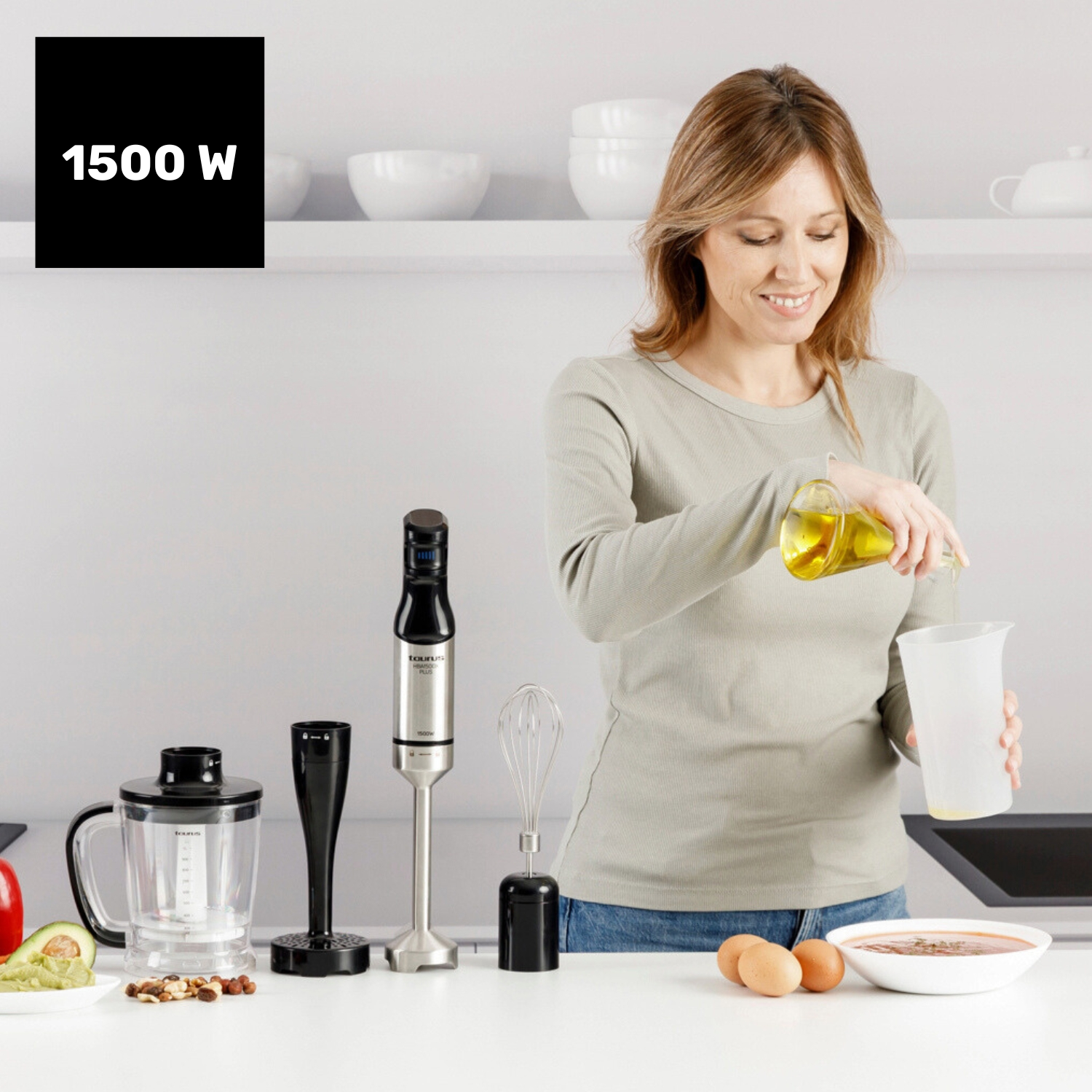 Mujer vertiendo aceite en una taza medidora. Batidora, batidor y otros utensilios de cocina sobre la mesa. Huevos y un plato con sopa presentes.