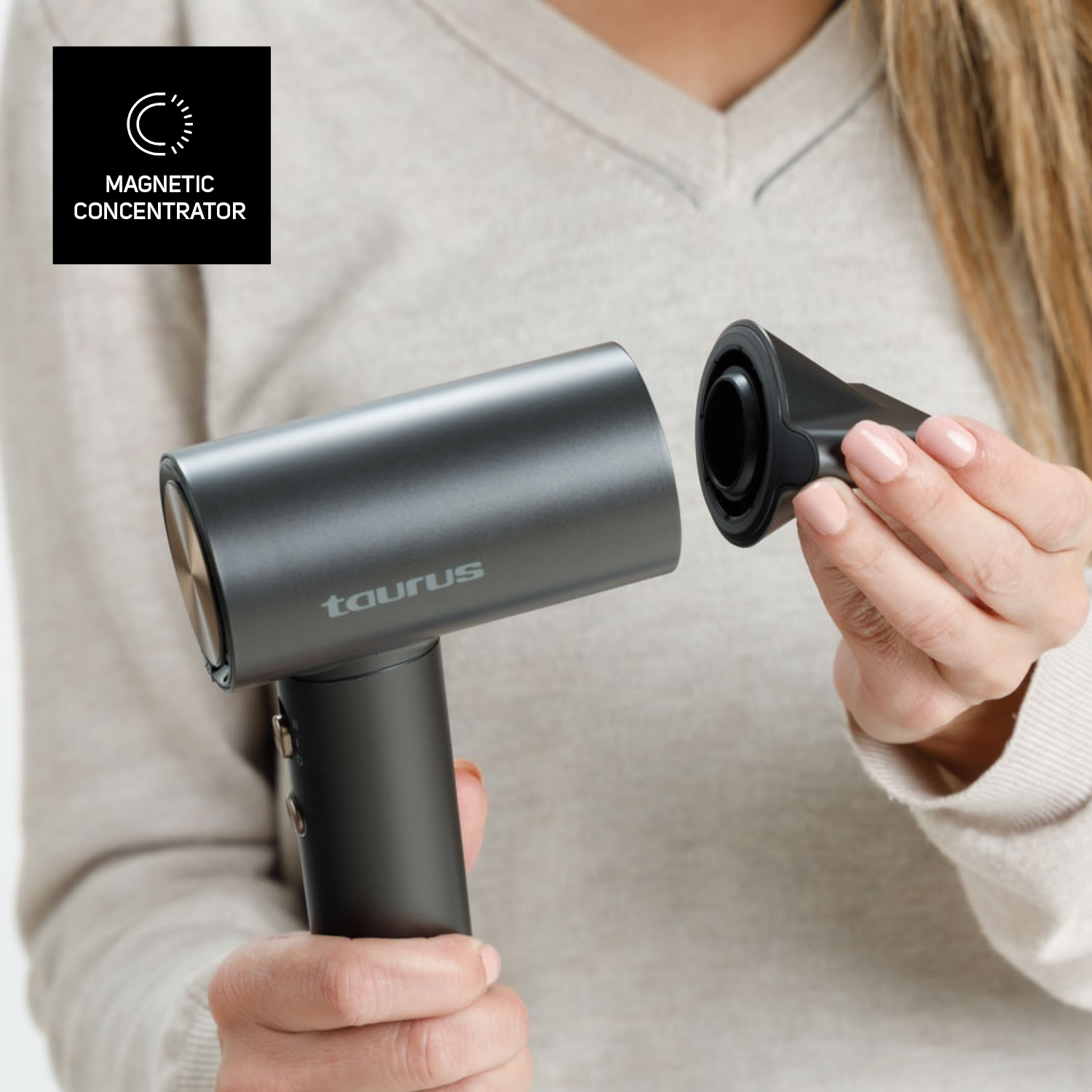 Una mujer sostiene un secador de pelo gris oscuro con una boquilla desmontable. El secador tiene el logo 'taurus'. Es visible una etiqueta de 'concentrador magnético'.