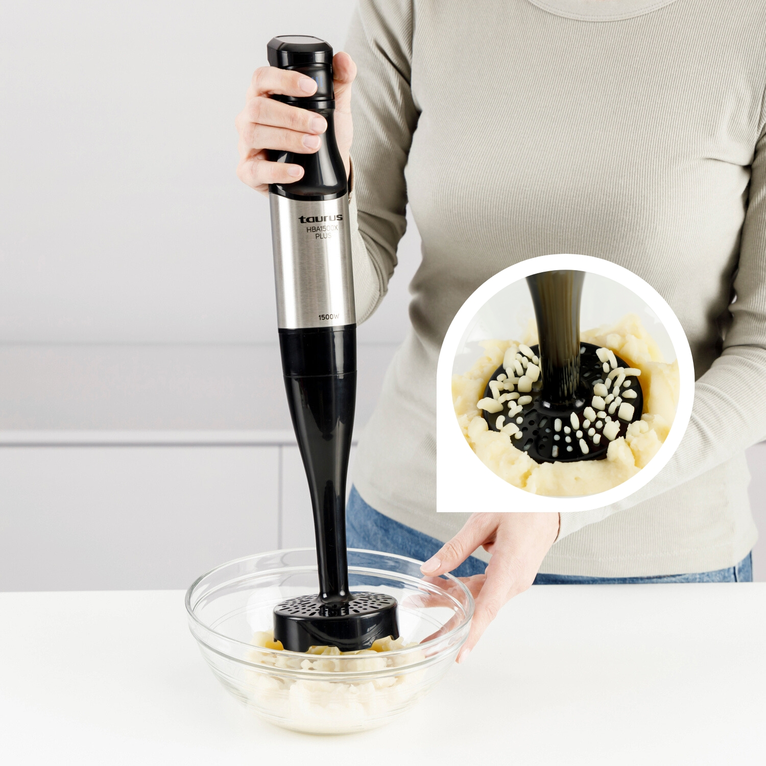 Una persona usa una batidora de mano negra y plateada para mezclar ingredientes en un bol de cristal. Los ingredientes parecen puré de patatas y una salsa oscura.