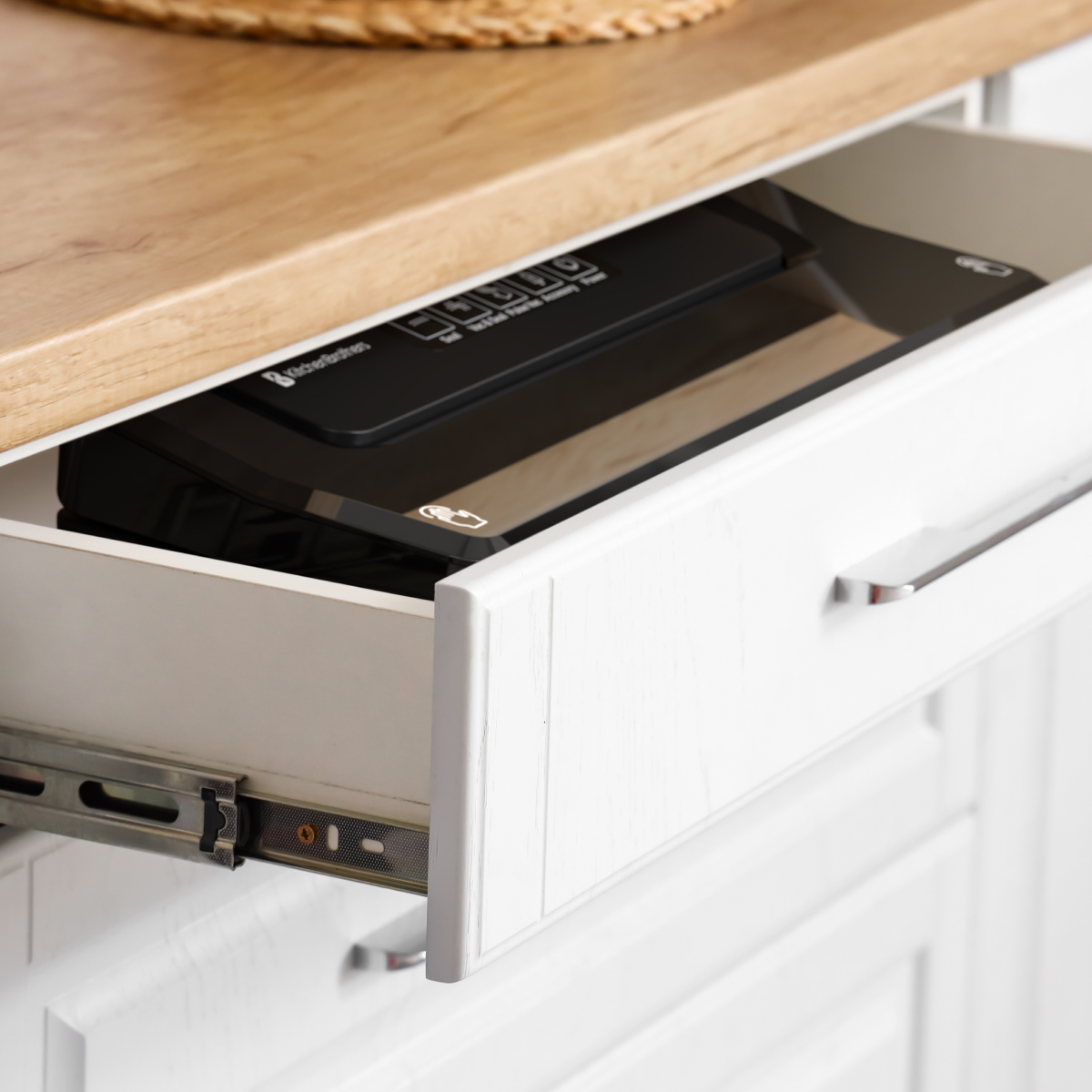 A white drawer is partially open, revealing a black appliance. Above is a wooden countertop and a woven basket.