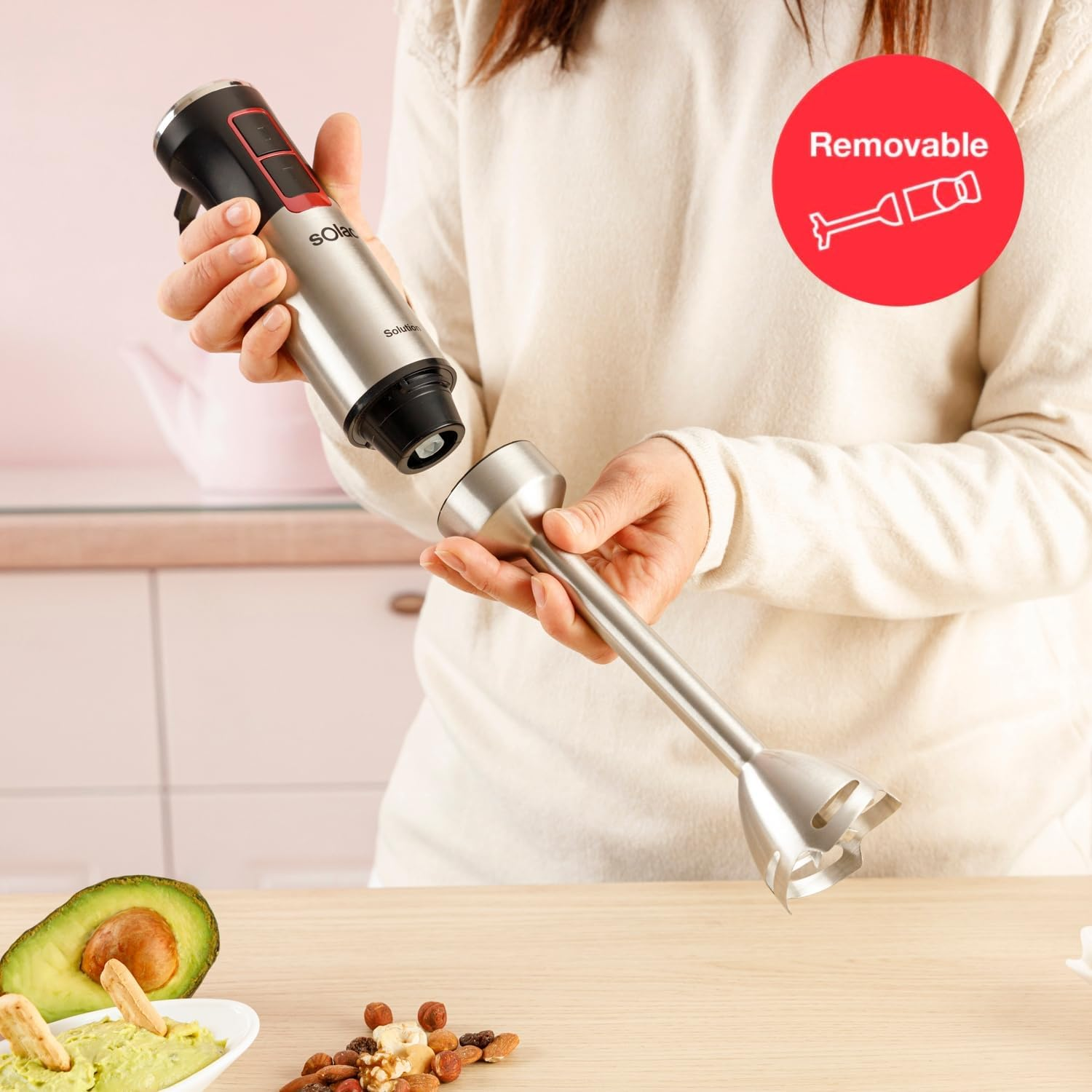 Una persona desmonta una batidora de mano plateada y negra. Guacamole, aguacate y nueces sobre una mesa de madera.