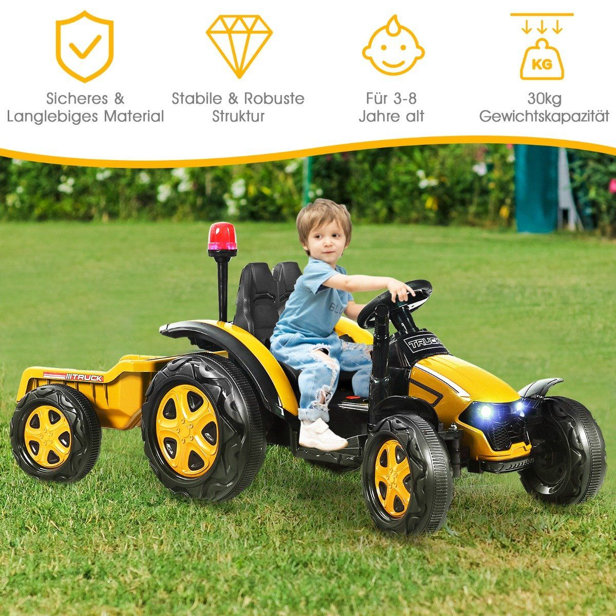 Un niño pequeño está sentado en un tractor de juguete amarillo y negro sobre un césped verde. El tractor tiene un remolque.