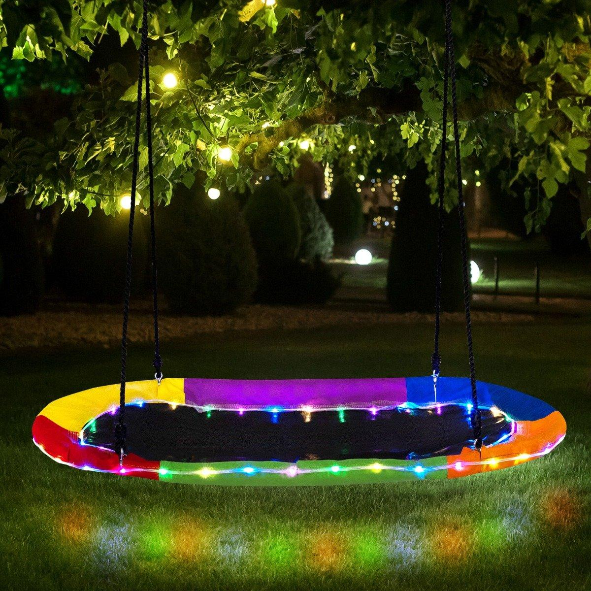 Un columpio colorido con luces cuelga de un árbol. El columpio tiene un asiento de malla negra y está iluminado con luces de colores.