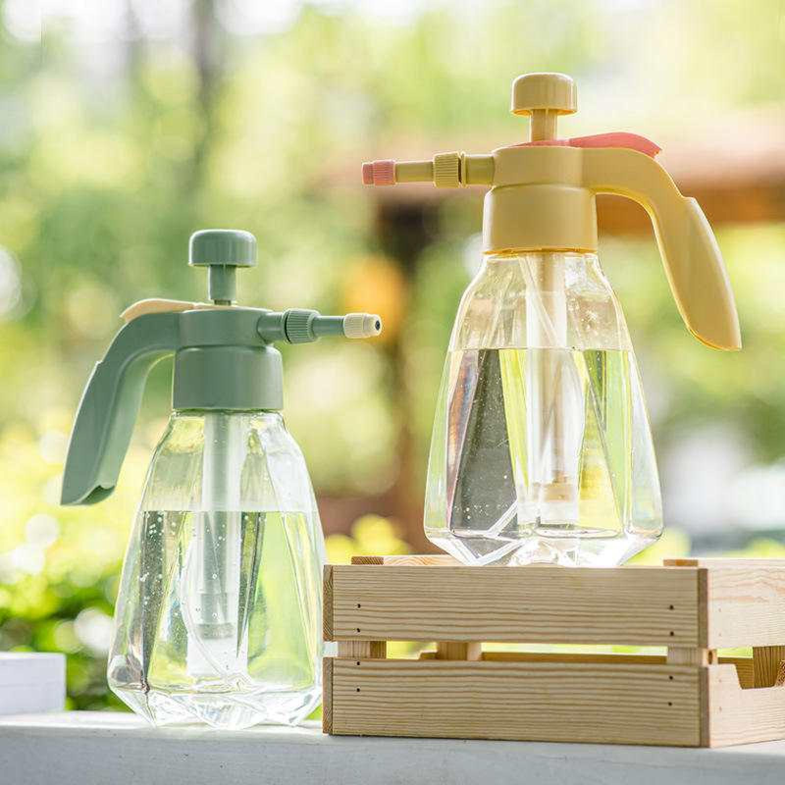 Zwei klare Sprühflaschen mit Wasser, eine grün, eine gelb, auf einer Holzkiste vor grünem Hintergrund.
