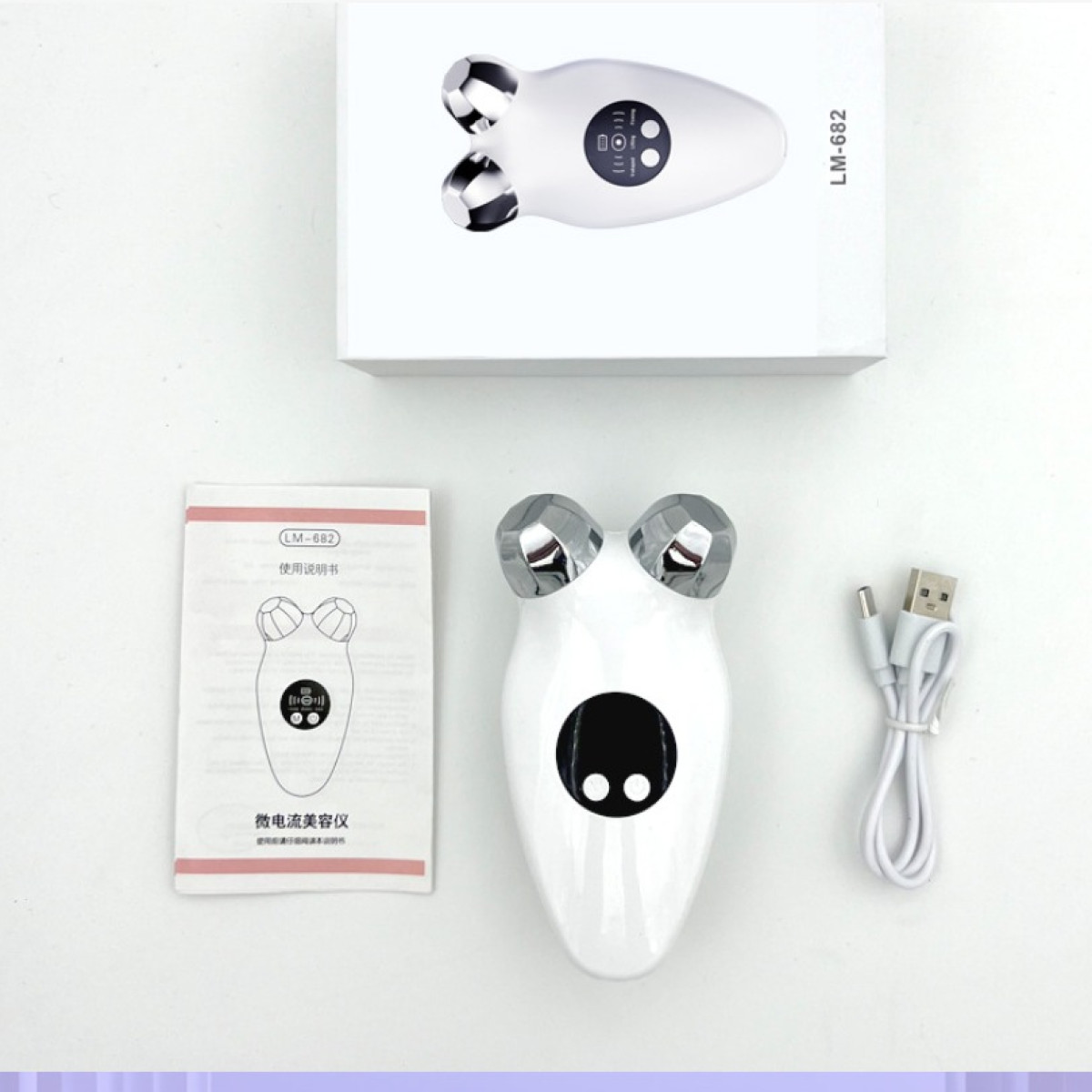 Biały masażer do twarzy ze srebrnymi głowicami, pudełko, instrukcja i kabel USB na białej powierzchni. Masażer ma czarny panel sterowania.