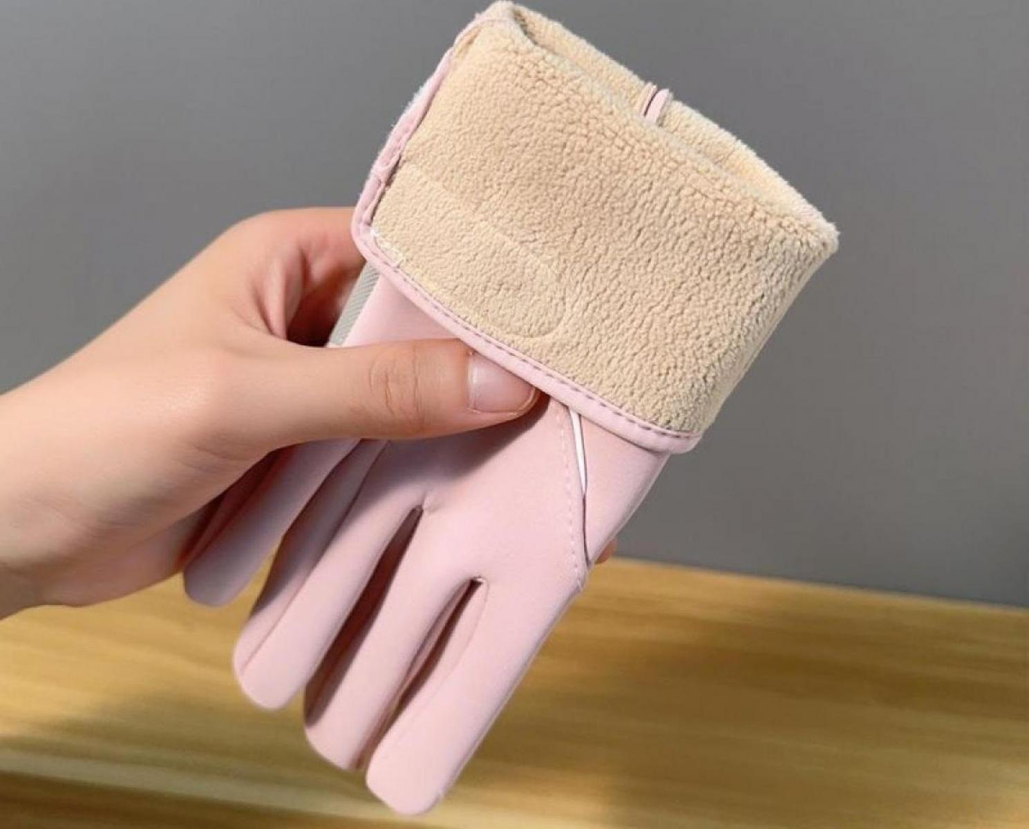 Eine Hand hält einen rosa Handschuh mit beigefarbenem, flauschigem Bündchen. Der Hintergrund ist ein verschwommenes, neutrales Grau.