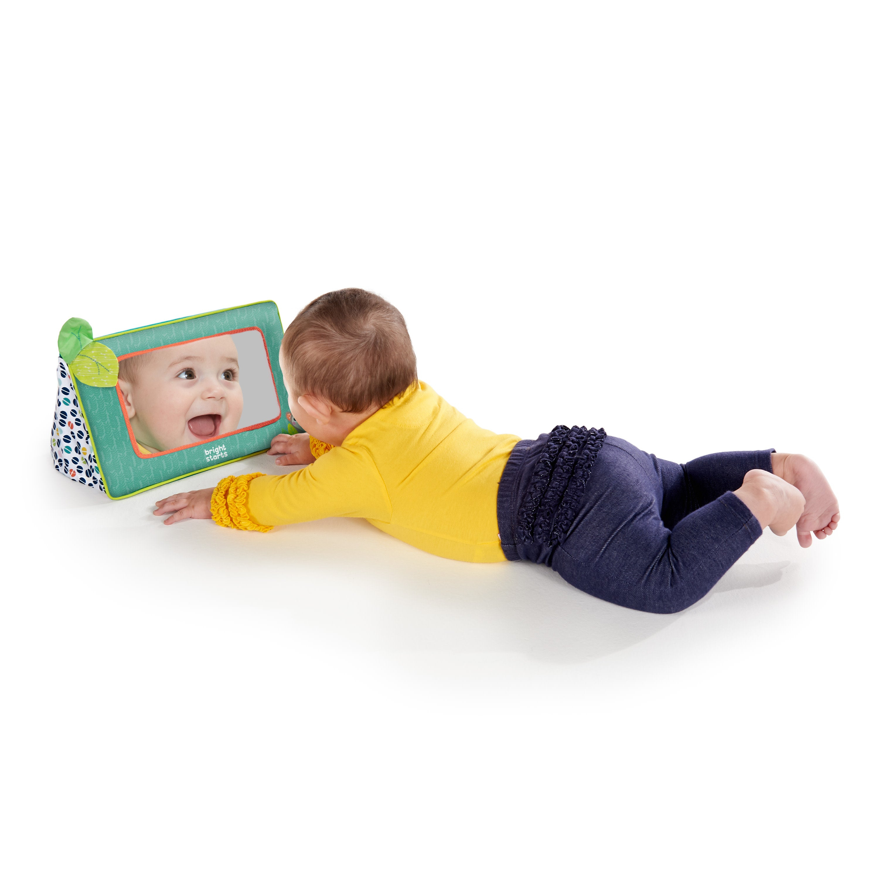 Baby liegt und schaut in einen Spiegel. Das Baby lächelt. Der Spiegel ist grün und hat ein Blatt.
