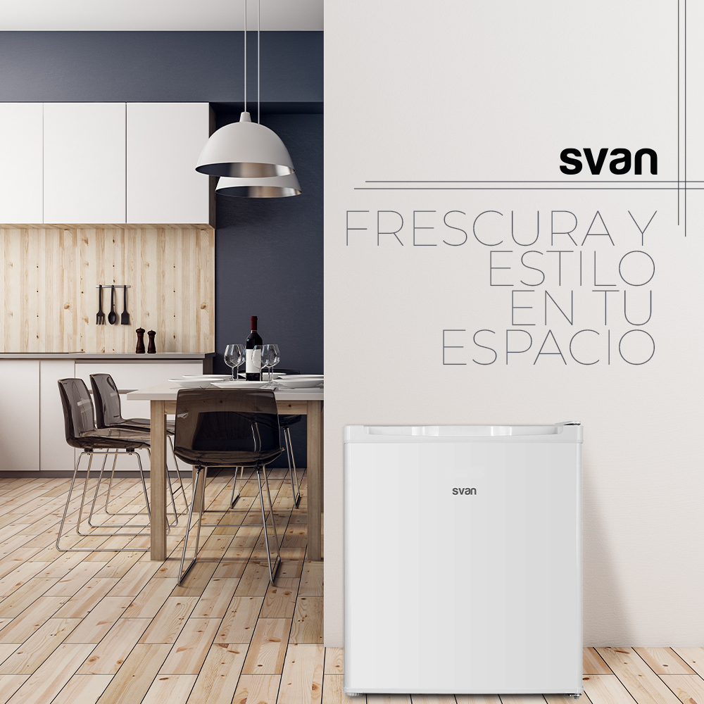 Un refrigerador blanco en un entorno de cocina. Una mesa con sillas, vino y copas en el fondo.