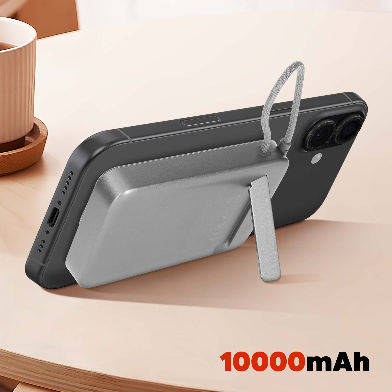Ein schwarzes Telefon mit einer silbernen Powerbank. Der Ständer hält es. Im Hintergrund eine Tasse.