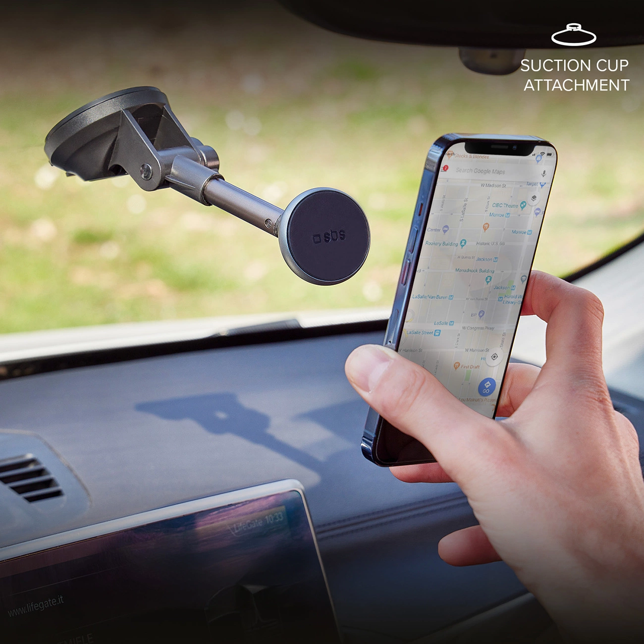 Una mano che tiene un telefono che mostra una mappa, vicino al cruscotto di un'auto. Un supporto per telefono a ventosa è montato sul parabrezza.