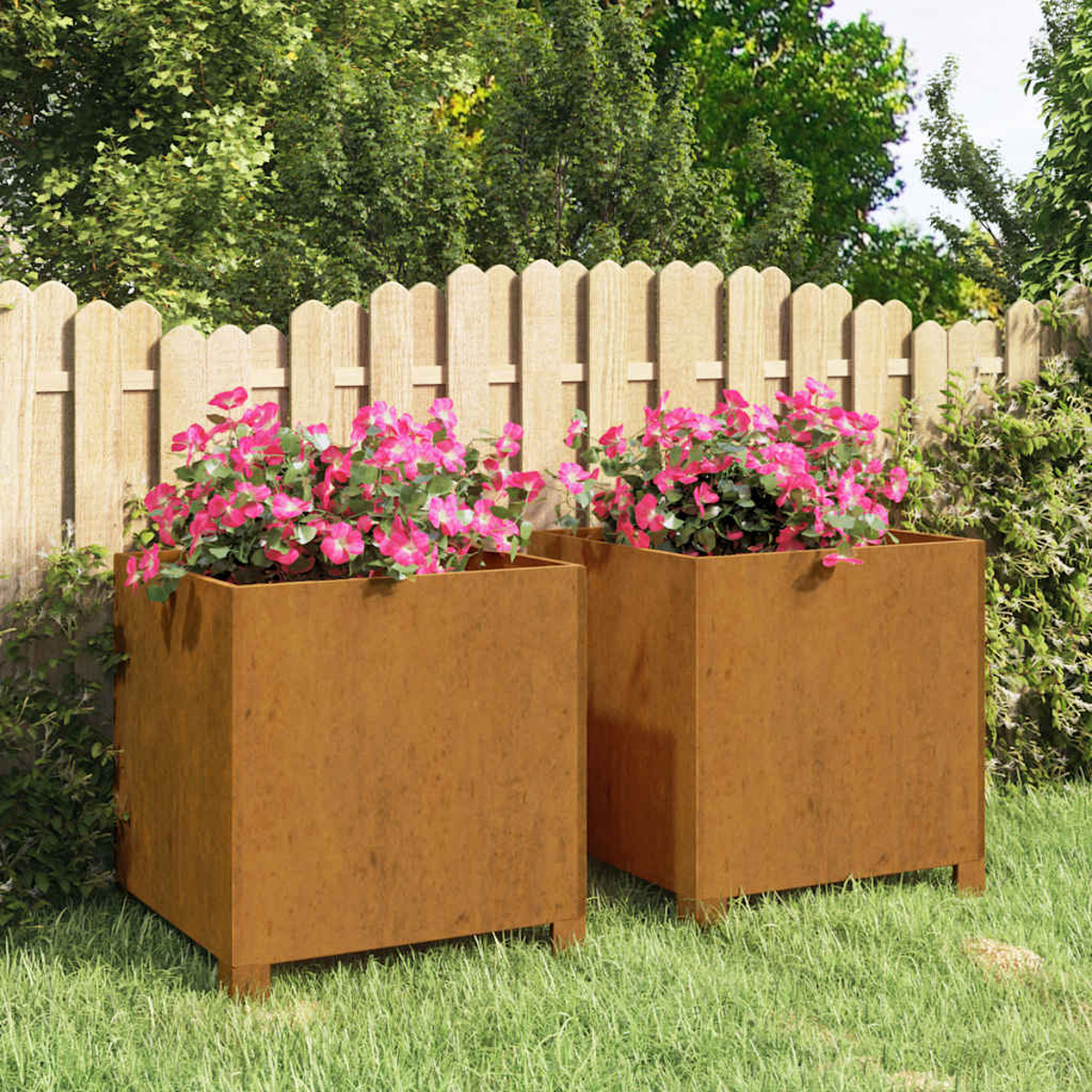 Zwei quadratische, rostfarbene Pflanzgefäße mit rosa Blüten stehen auf Gras. Im Hintergrund ein Holzzaun und grüne Bäume.