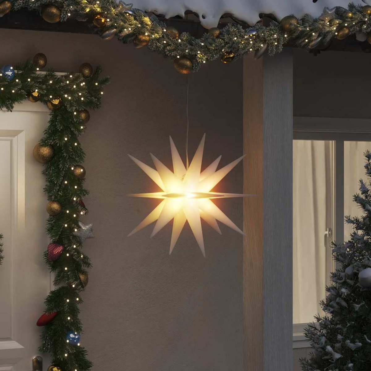 Ein leuchtendes sternförmiges Licht hängt draußen an einem Gebäude, das für Weihnachten geschmückt ist. Girlanden und ein kleiner Baum sind ebenfalls zu sehen.