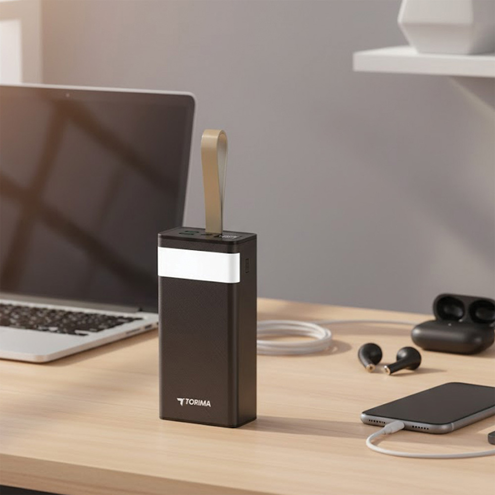 Bej renkli bir tutamağı olan bir powerbank ahşap bir masanın üzerinde duruyor. Bir dizüstü bilgisayar, kulaklıklar, telefon ve şarj kablosu da görünür.