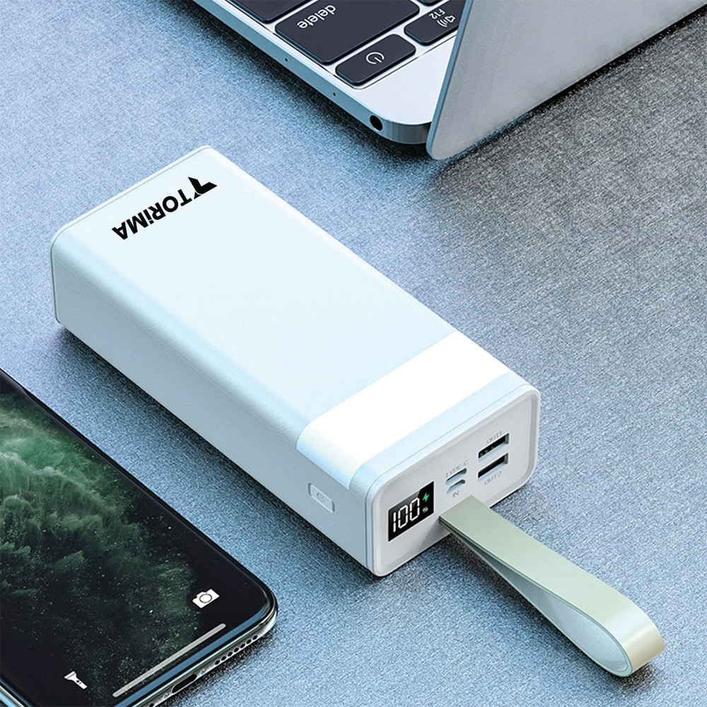 Torima logolu beyaz bir powerbank, bir telefon ve bir dizüstü bilgisayar gri bir yüzeyde. Powerbank %100 şarj gösteriyor.