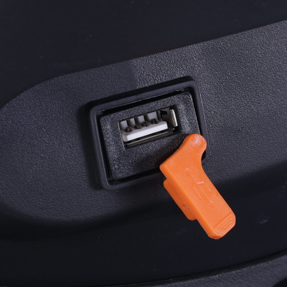 Zbliżenie czarnego portu USB z białym wkładem. Pomarańczowa osłona ochronna jest częściowo włożona. Tło jest czarne.