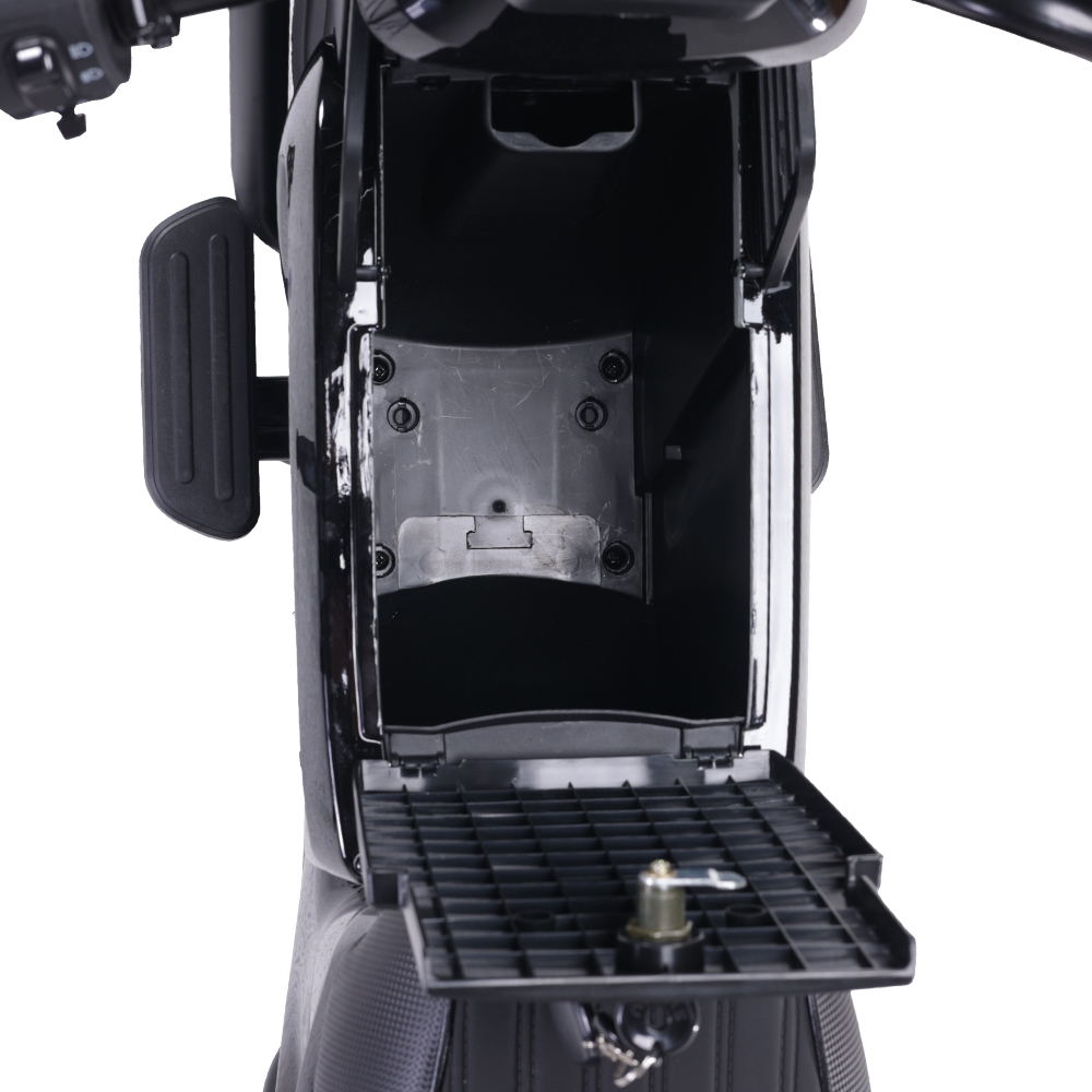 Otwarty czarny schowek na skuter, odsłaniający wnętrze. Klucz w zamku. Podnóżek i kierownica widoczne. Białe tło.