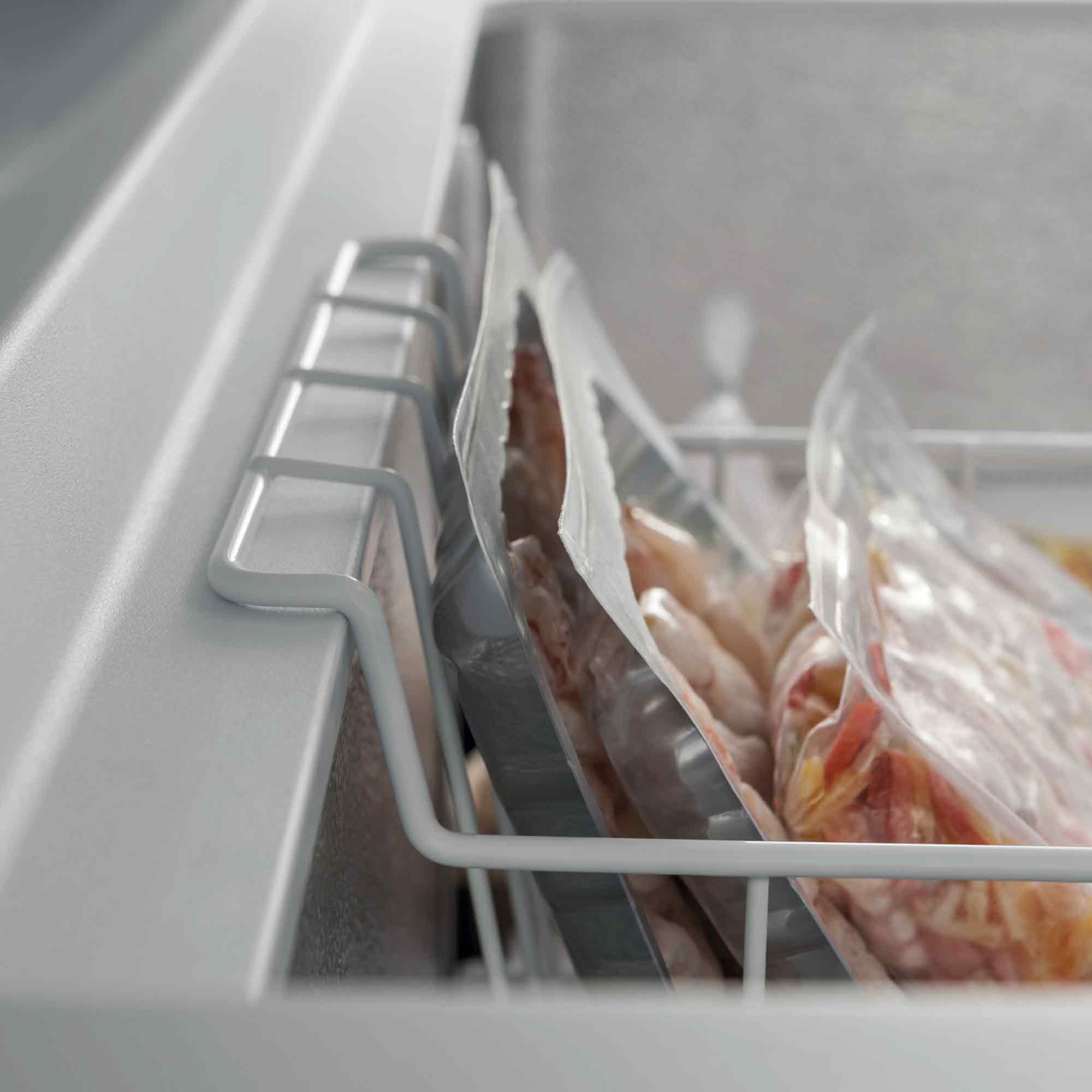 Gefrierfachinnenraum mit gefrorenen Lebensmitteltüten in einem weißen Drahtgestell. Die Tüten enthalten Lebensmittel.