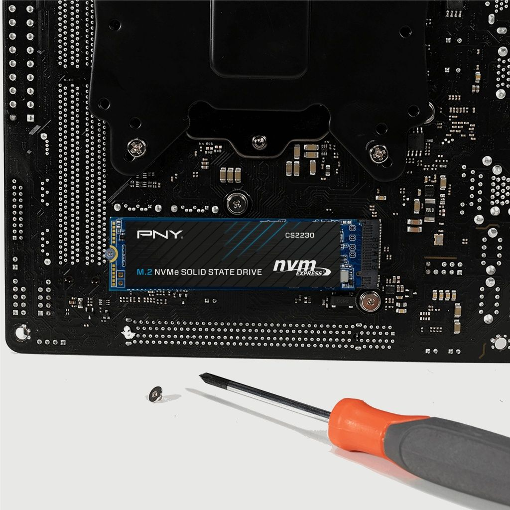 Una scheda madre per computer con un SSD M.2 NVMe installato. Un cacciavite e una vite su una superficie bianca.