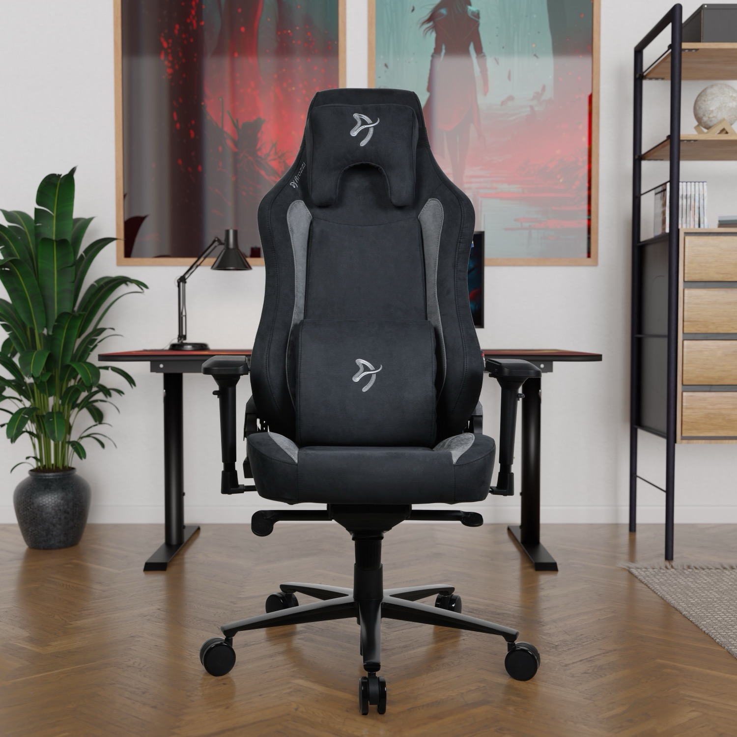 Een zwarte gamestoel staat centraal. Een bureau met een monitor staat erachter. Kunstwerken en een boekenplank op de achtergrond.