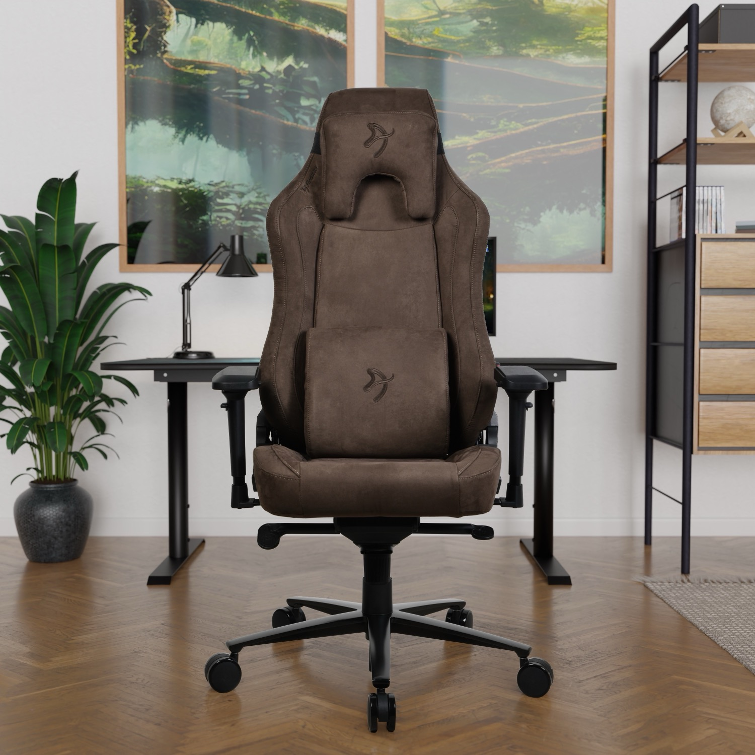 Ein brauner Gaming-Stuhl steht vor einem Schreibtisch. Im Hintergrund befinden sich eine Pflanze, eine Schreibtischlampe und gerahmte Bilder.