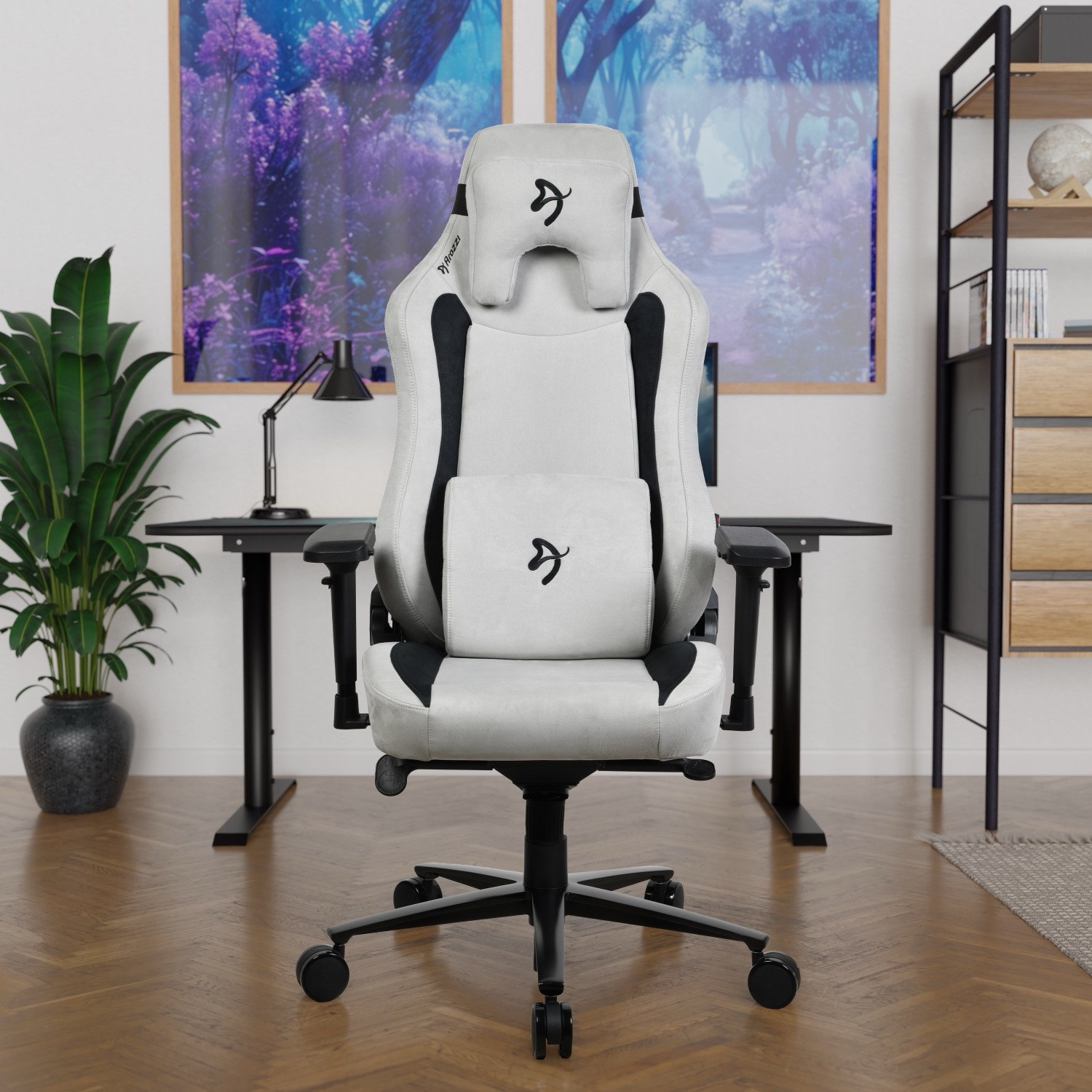 Ein weiß-schwarzer Gaming-Stuhl in einem Homeoffice. Ein Schreibtisch, eine Pflanze und Kunstwerke sind im Hintergrund zu sehen.