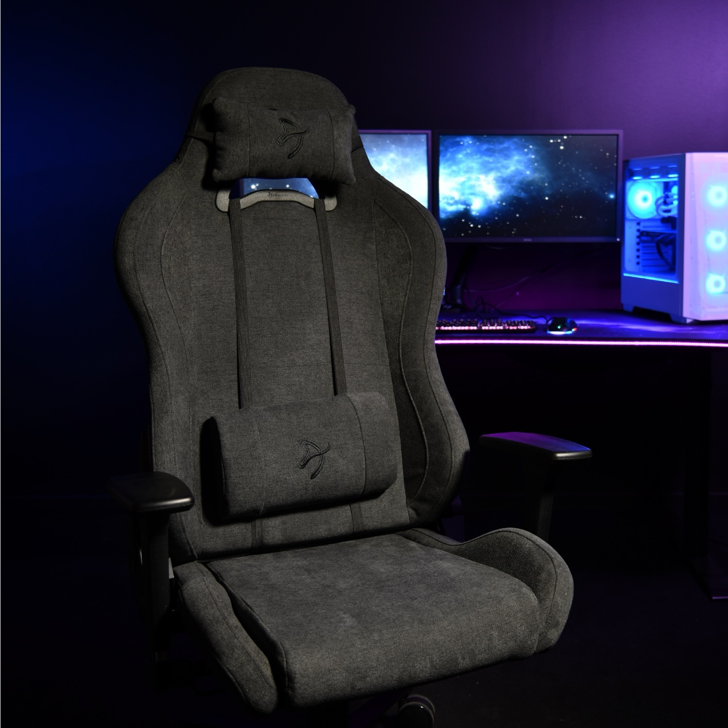 Gaming stoel in een donkere kamer. Grijze stoel met hoofdsteun en lendensteun. Computermonitoren en een witte pc-kast op de achtergrond.