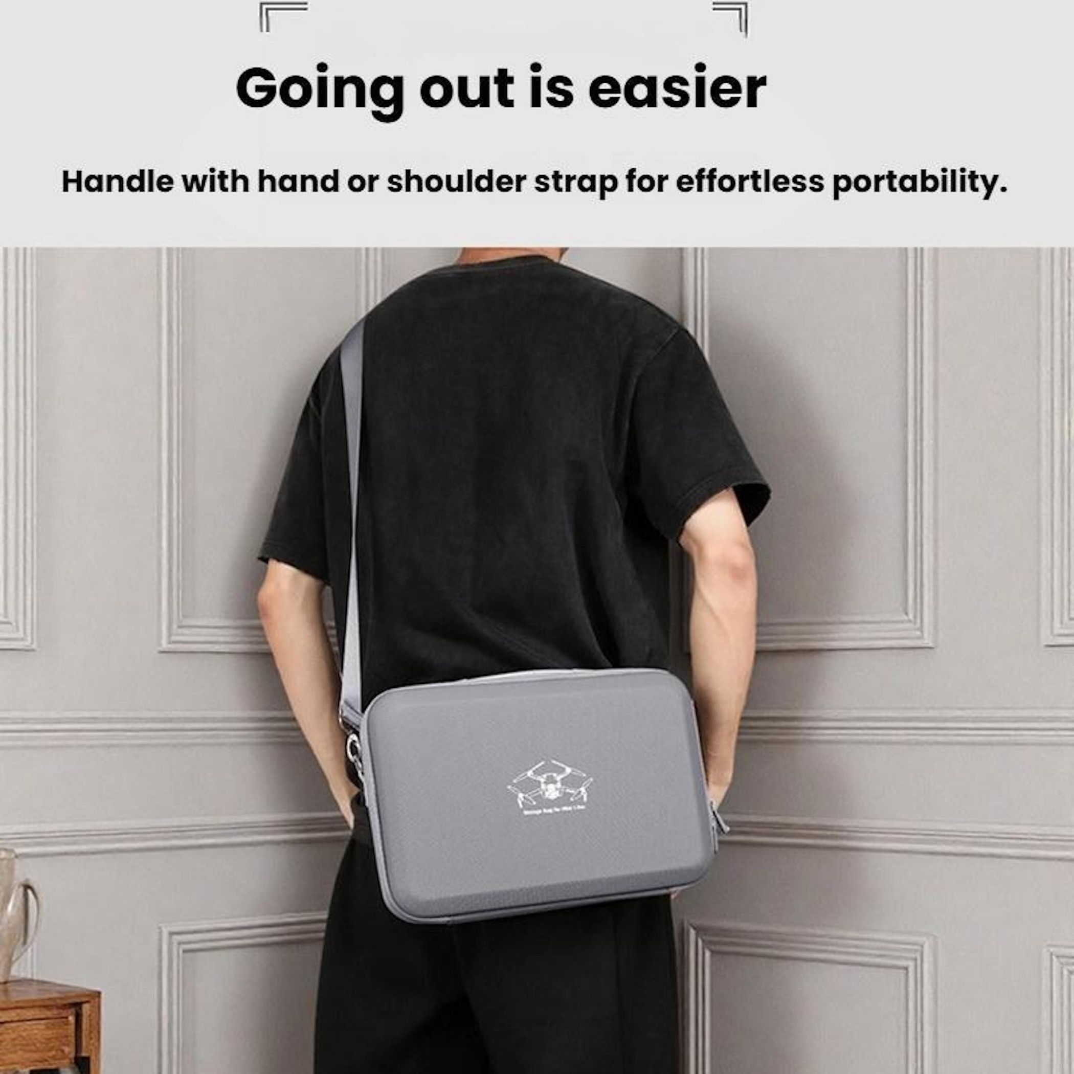Eine Person trägt eine graue Tasche mit Schultergurt. Die Tasche hat ein Logo. Der Hintergrund ist eine hellgraue Wand.