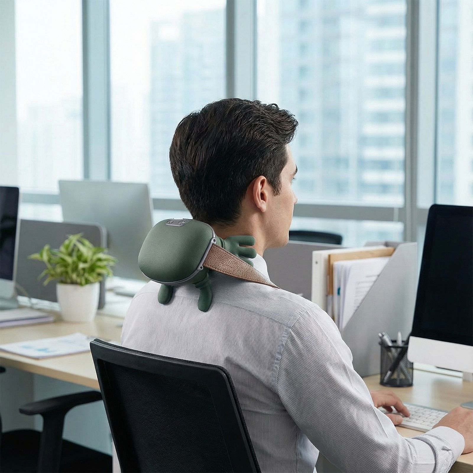 Mann am Schreibtisch mit Nackenmassagegerät. Büroumgebung mit Computern und Pflanzen. Er tippt auf einer Tastatur.