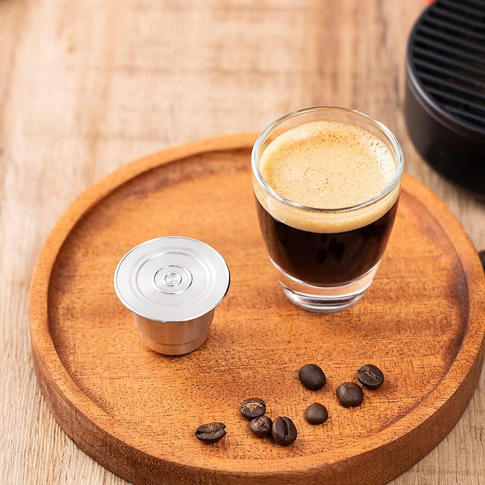 Ein Espresso im Glas, eine Kaffeekapsel und Kaffeebohnen auf einem Holztablett. Der Hintergrund ist unscharf.