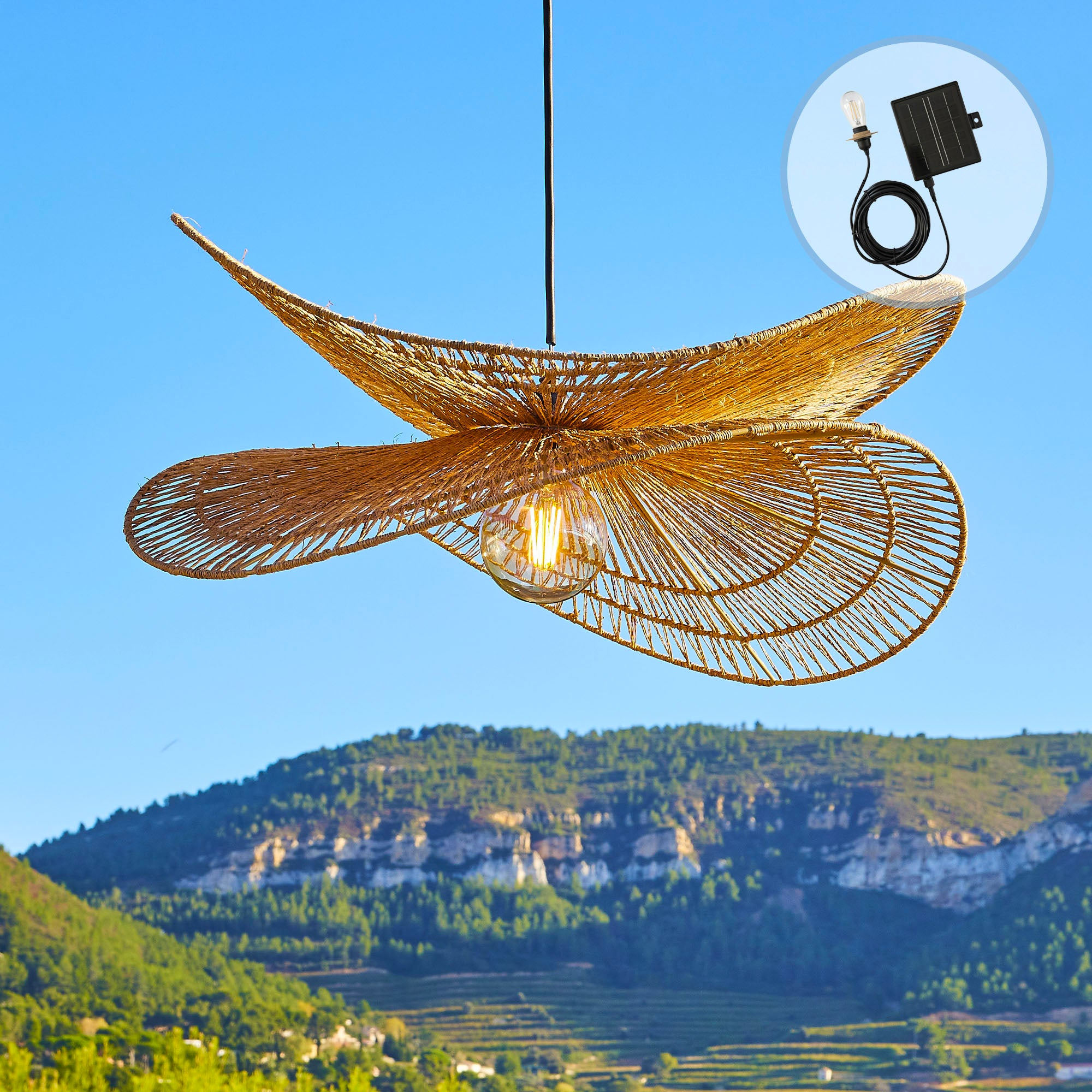 Ein gewebter Lampenschirm mit einer Glühbirne hängt vor blauem Himmel, Berge im Hintergrund und ein Solarpanel an der Seite.