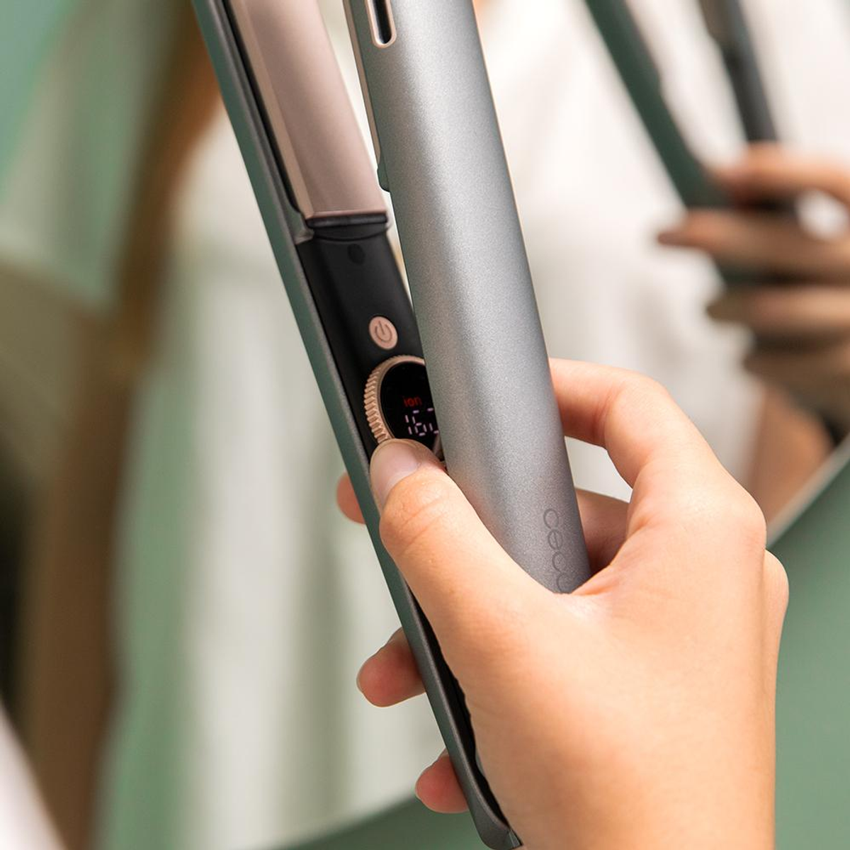 A person holding a gray hair straightener, the display shows 167 degrees. The background is slightly blurred.
