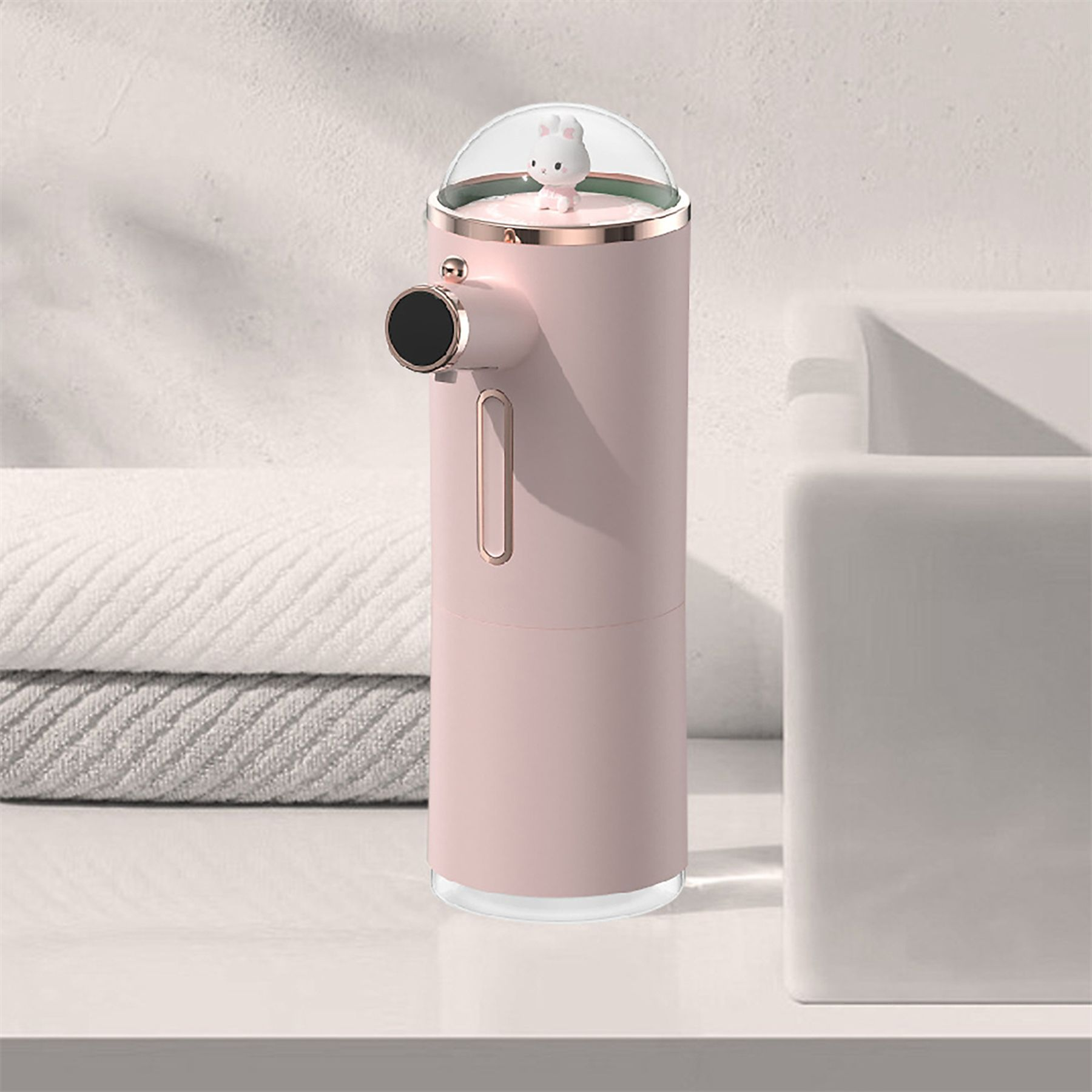 Ein rosa automatischer Seifenspender mit einem Hasen oben, neben Handtüchern und einem Waschbecken.