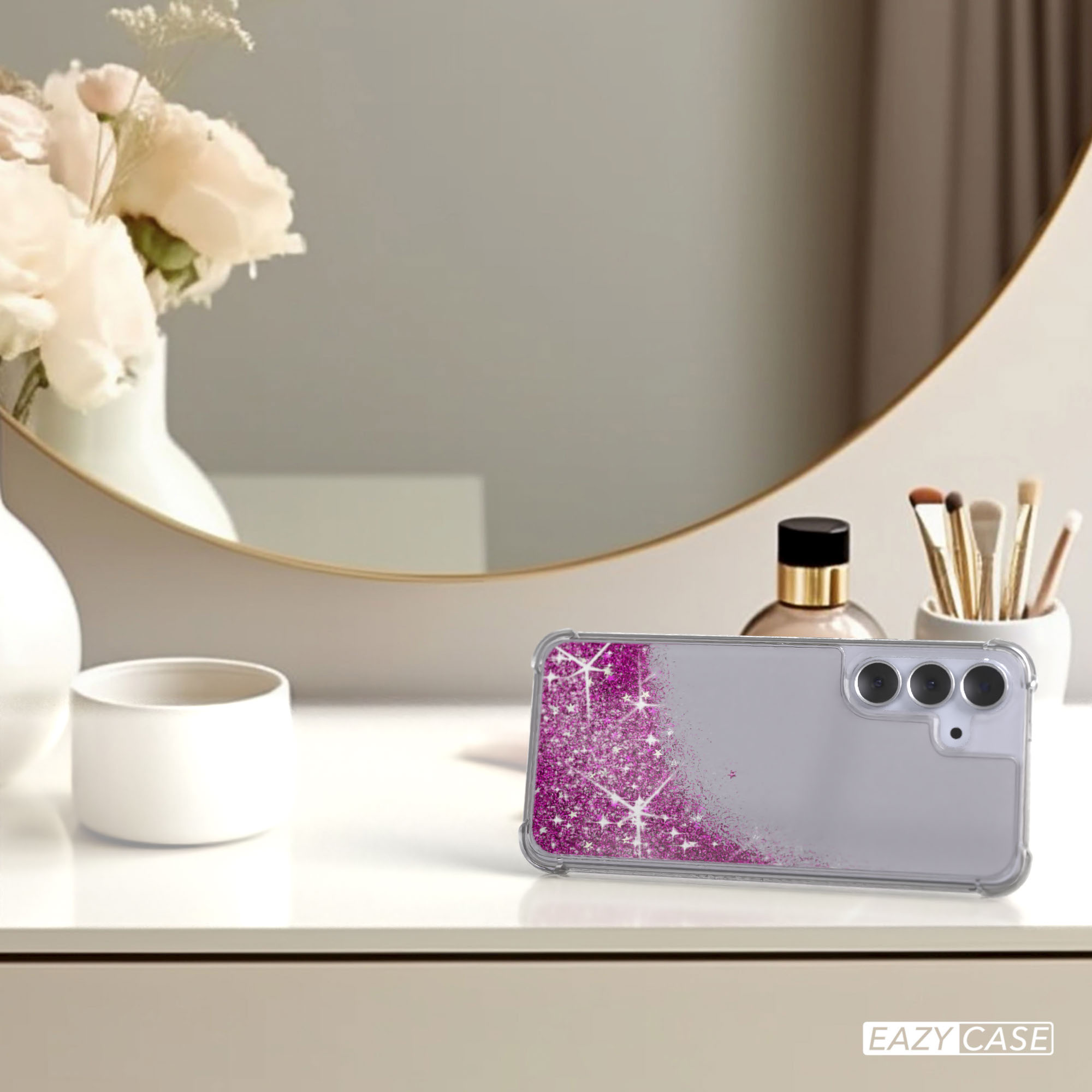 Eine Handyhülle mit pinkfarbenem Glitzer liegt auf einer weißen Oberfläche. Blumen, Spiegel und Make-up-Pinsel im Hintergrund.