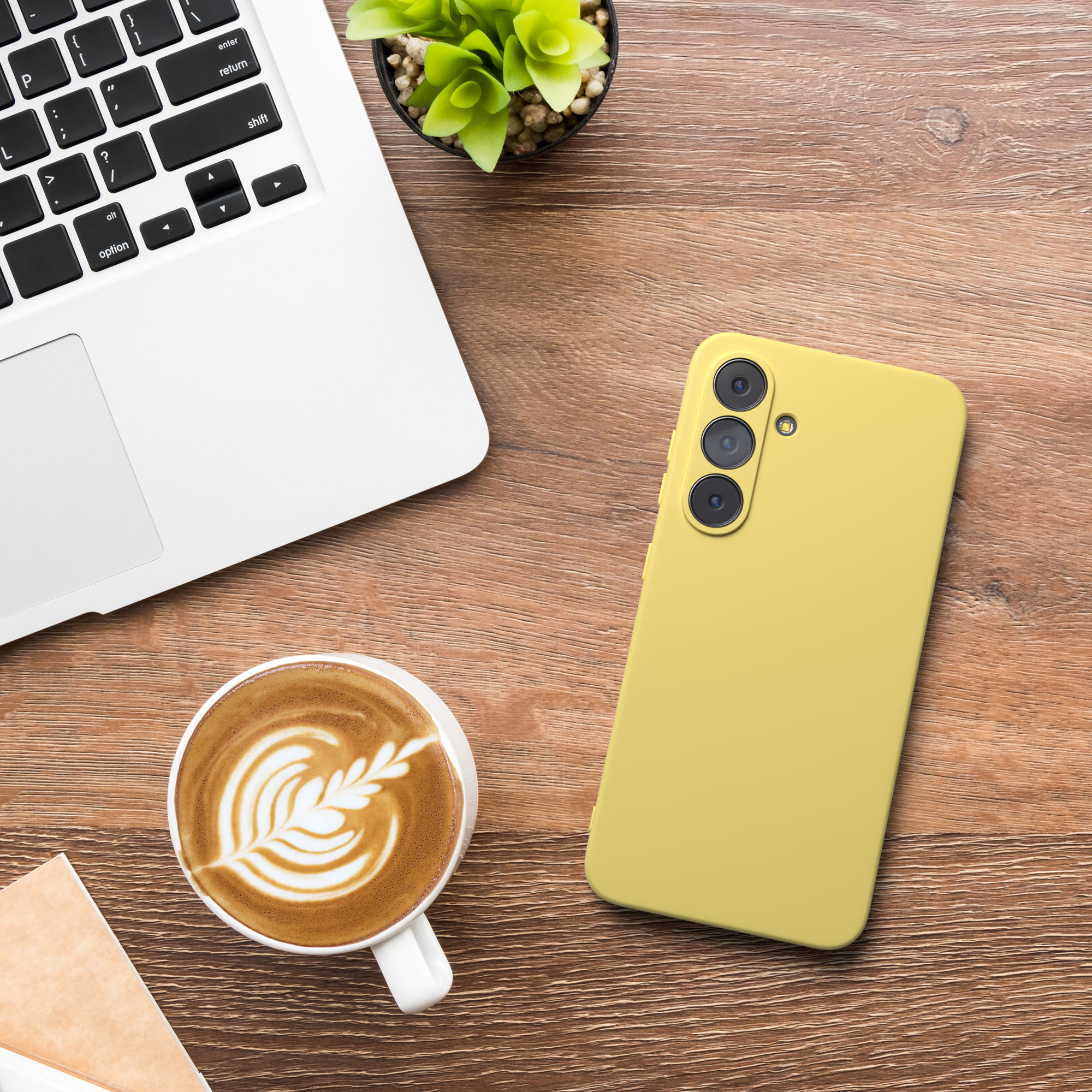Ein Laptop, gelbes Telefon, Kaffee mit Latte Art und eine kleine Pflanze auf einem Holzschreibtisch.