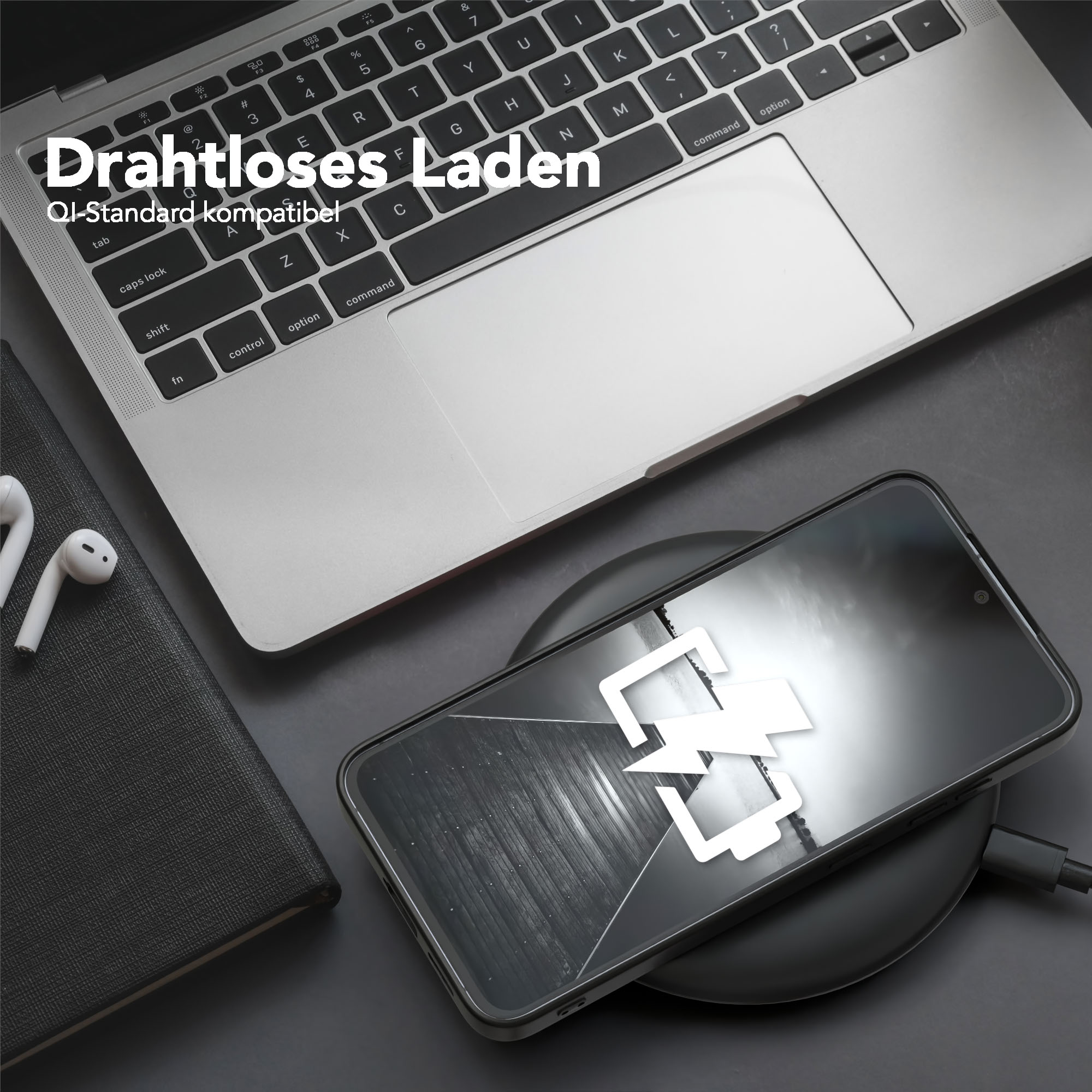 Telefon wird auf einem kabellosen Ladegerät aufgeladen, neben einem Laptop und einem Notizbuch. Weiße Ohrhörer sind ebenfalls vorhanden.