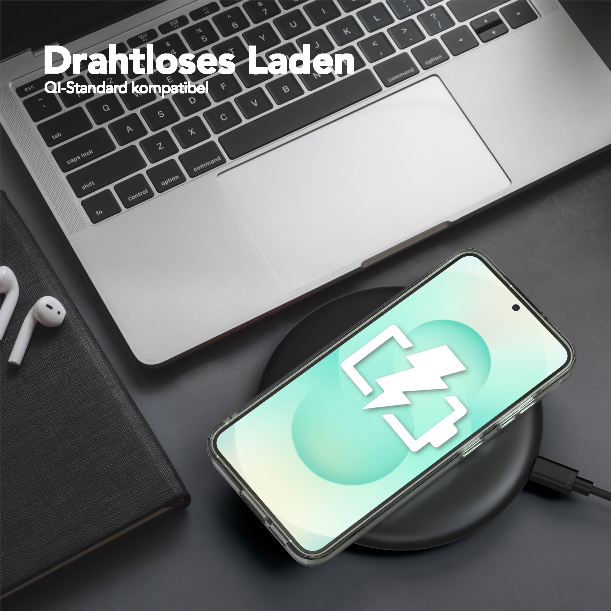 Ein Telefon, das drahtlos auf einem schwarzen Pad geladen wird, in der Nähe eines Laptops und Ohrhörern. Das Telefon zeigt ein Ladesymbol.