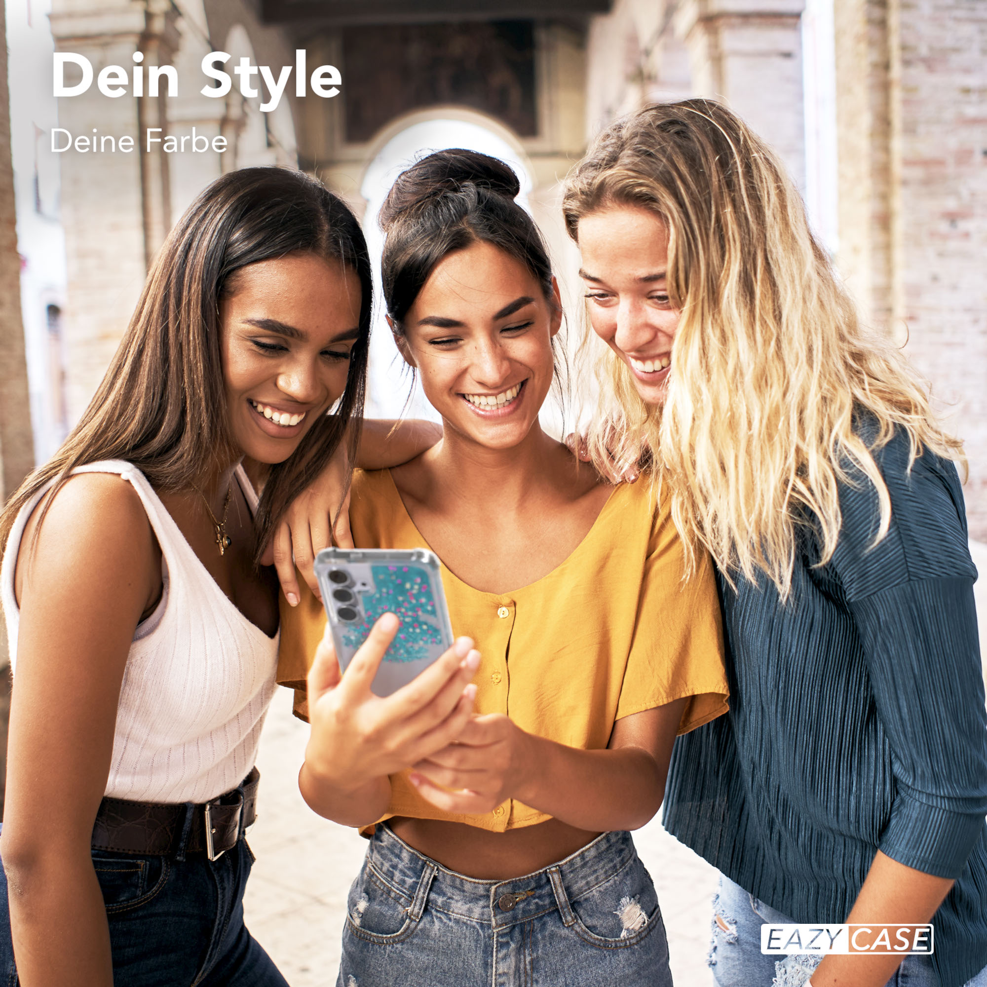 Drei Frauen schauen auf ein Telefon. Eine hält es. Sie lächeln. Der Hintergrund hat Torbögen. Text: 'Dein Style Deine Farbe'.