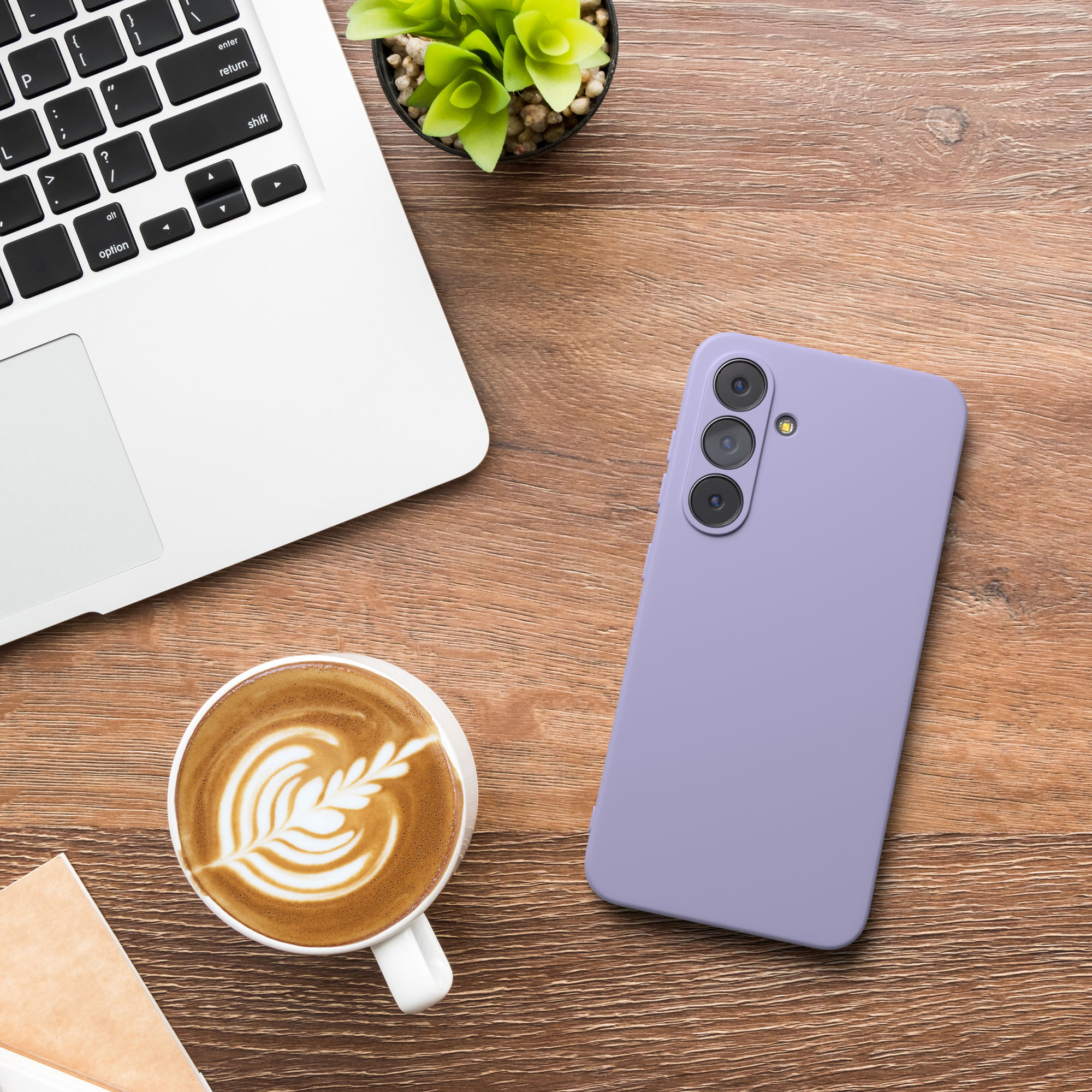 Auf einem Holztisch befinden sich ein Laptop, Kaffee mit Latte Art, ein lila Telefon und eine kleine Pflanze.