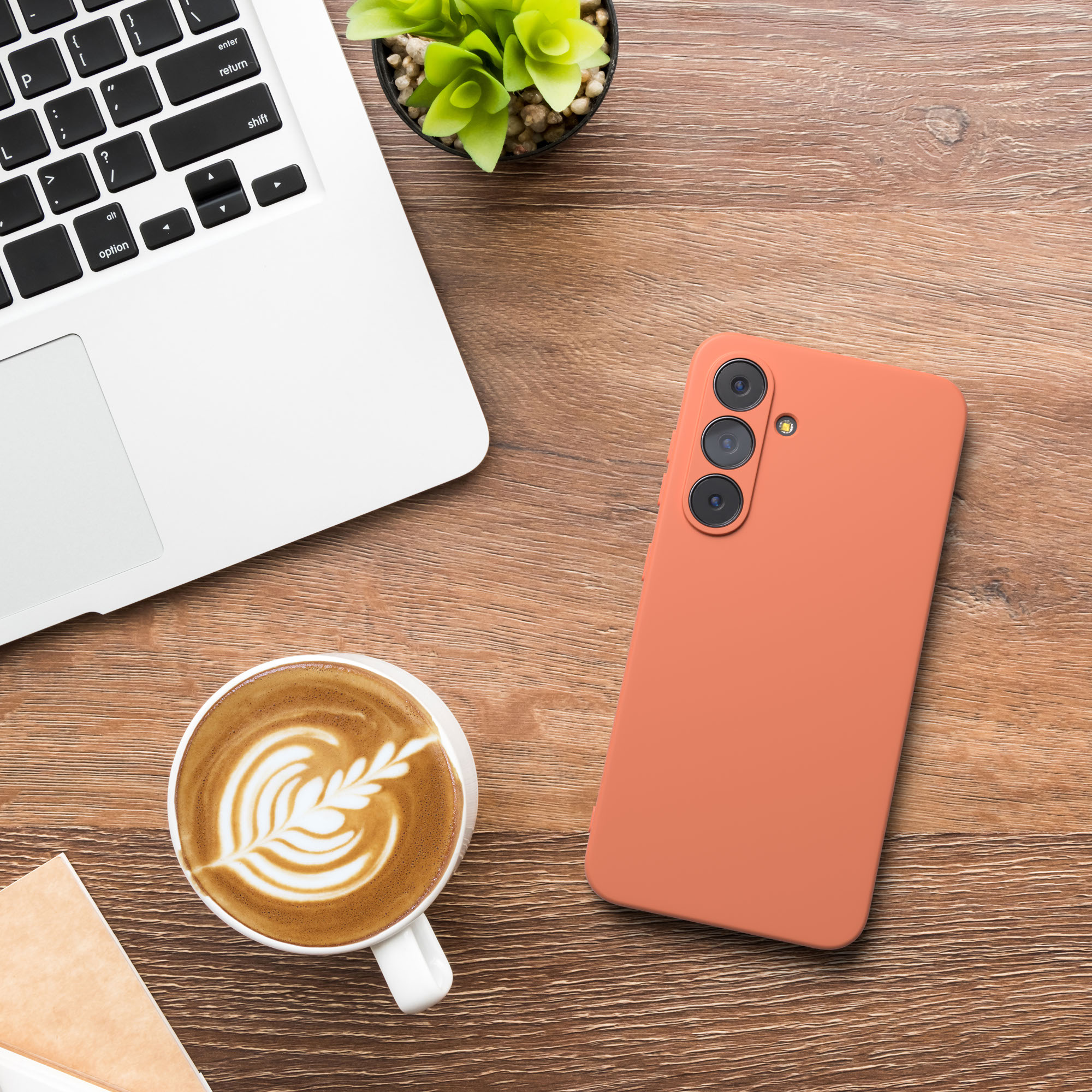 Laptop, Telefon, Kaffee und Pflanze stehen auf einem Holztisch. Das Telefon ist korallenfarben.