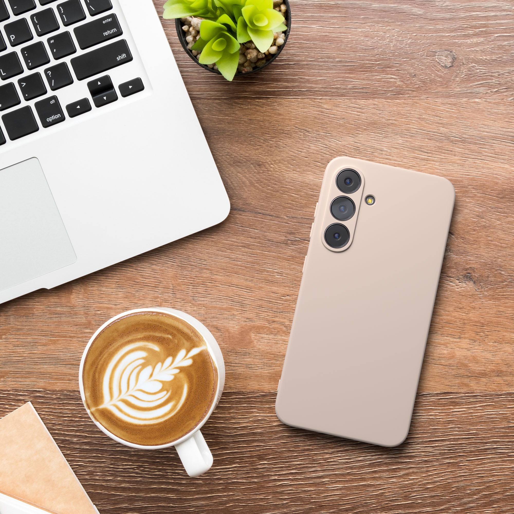 Ein Laptop, eine Kaffeetasse, ein Telefon und eine Pflanze stehen auf einem Holztisch. Kaffee-Kunst ist sichtbar.