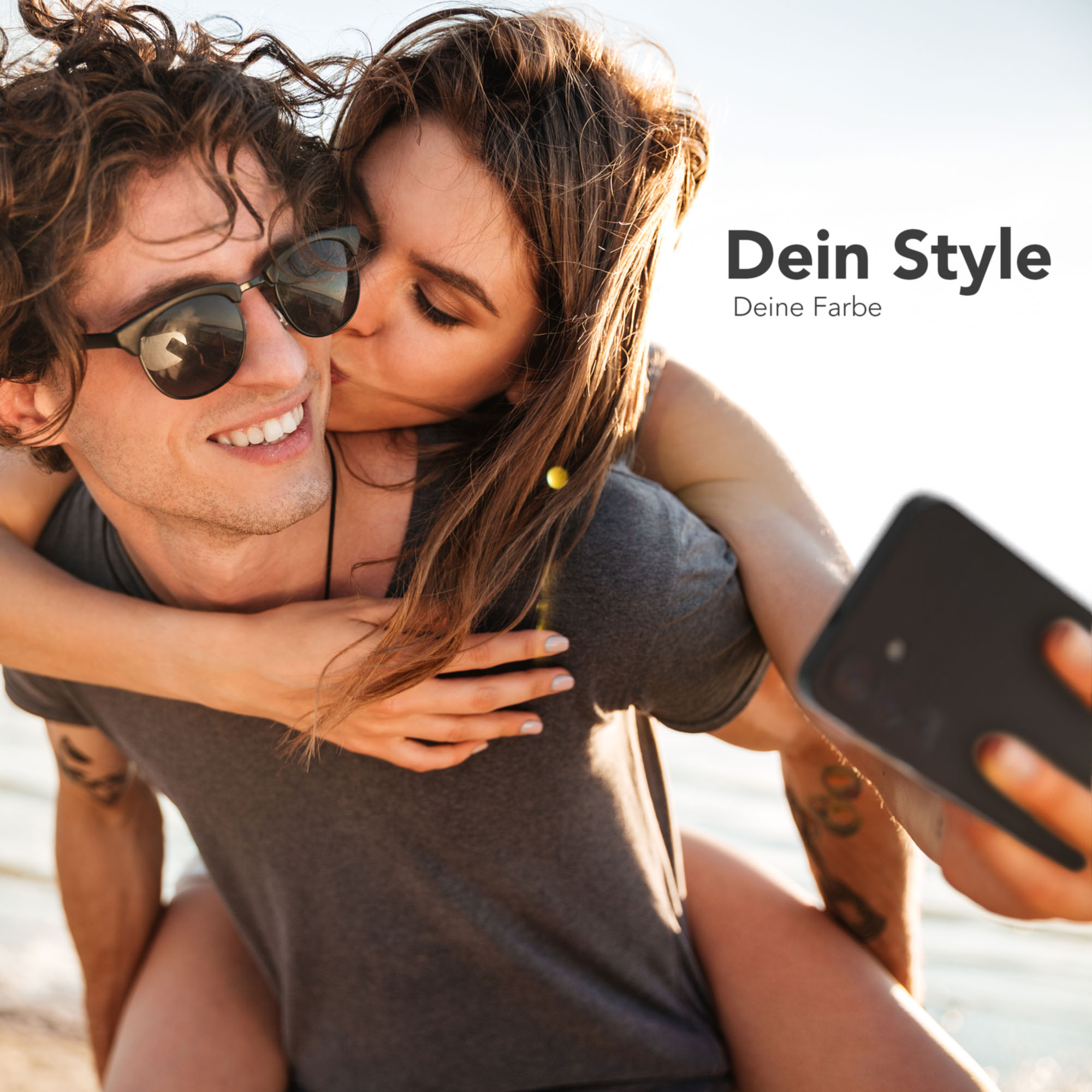 Ein Mann lächelt, während er von einer Frau von hinten geküsst wird. Beide machen ein Selfie mit einem Telefon.