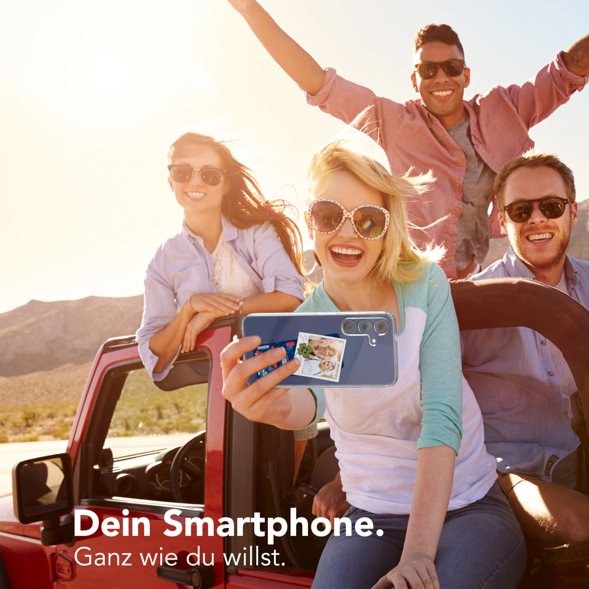 Gruppe von Freunden, die ein Selfie in einem roten Jeep machen. Die Sonne scheint hell. Text: Dein Smartphone. Ganz wie du willst.
