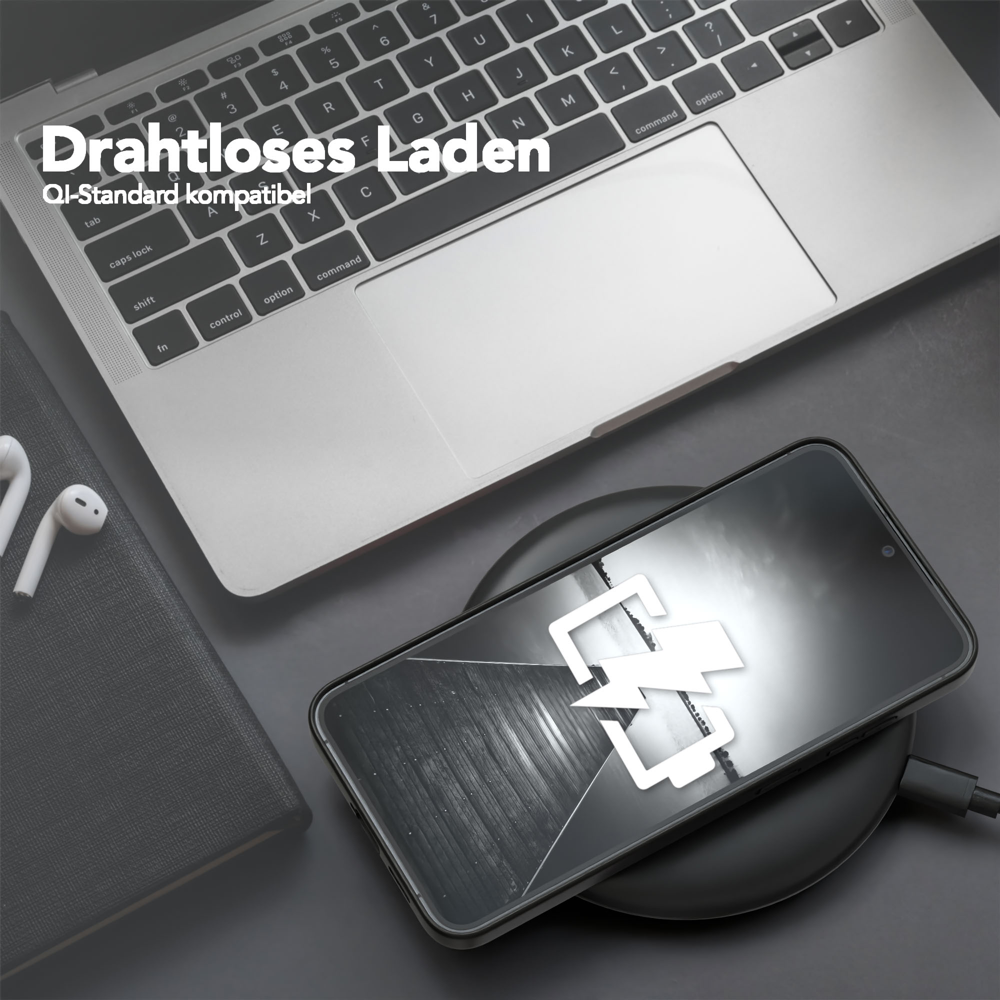 Ein Telefon auf einem kabellosen Ladegerät neben einem Laptop und Ohrhörern. Das Telefon zeigt ein Ladesymbol.