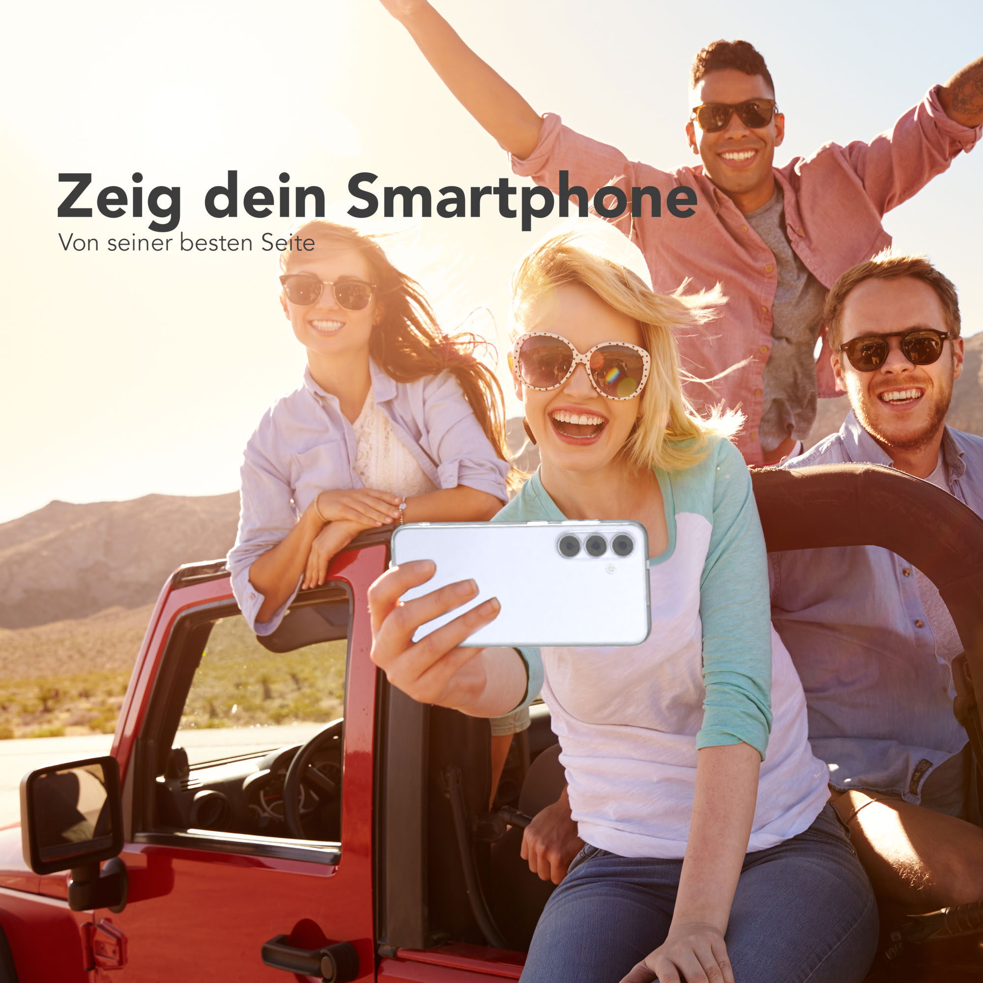 Freundesgruppe in einem roten Jeep, die ein Selfie mit einem Handy macht. Sonniger Hintergrund und Wüstenlandschaft.