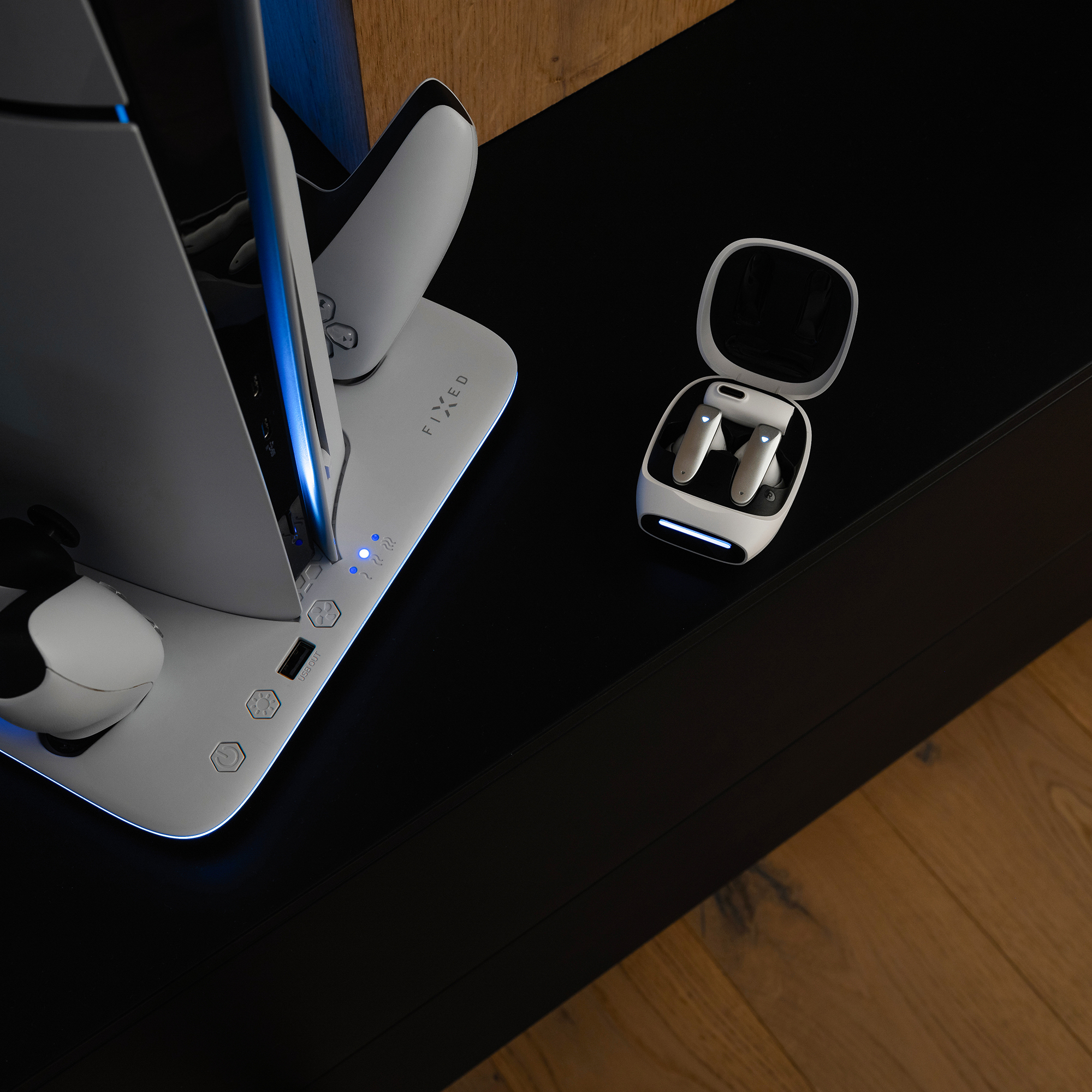 Weißes Gaming-Konsolenladegerät mit Controllern. Ohrhörer in einem Etui. Schwarzer Tisch, Holzboden.