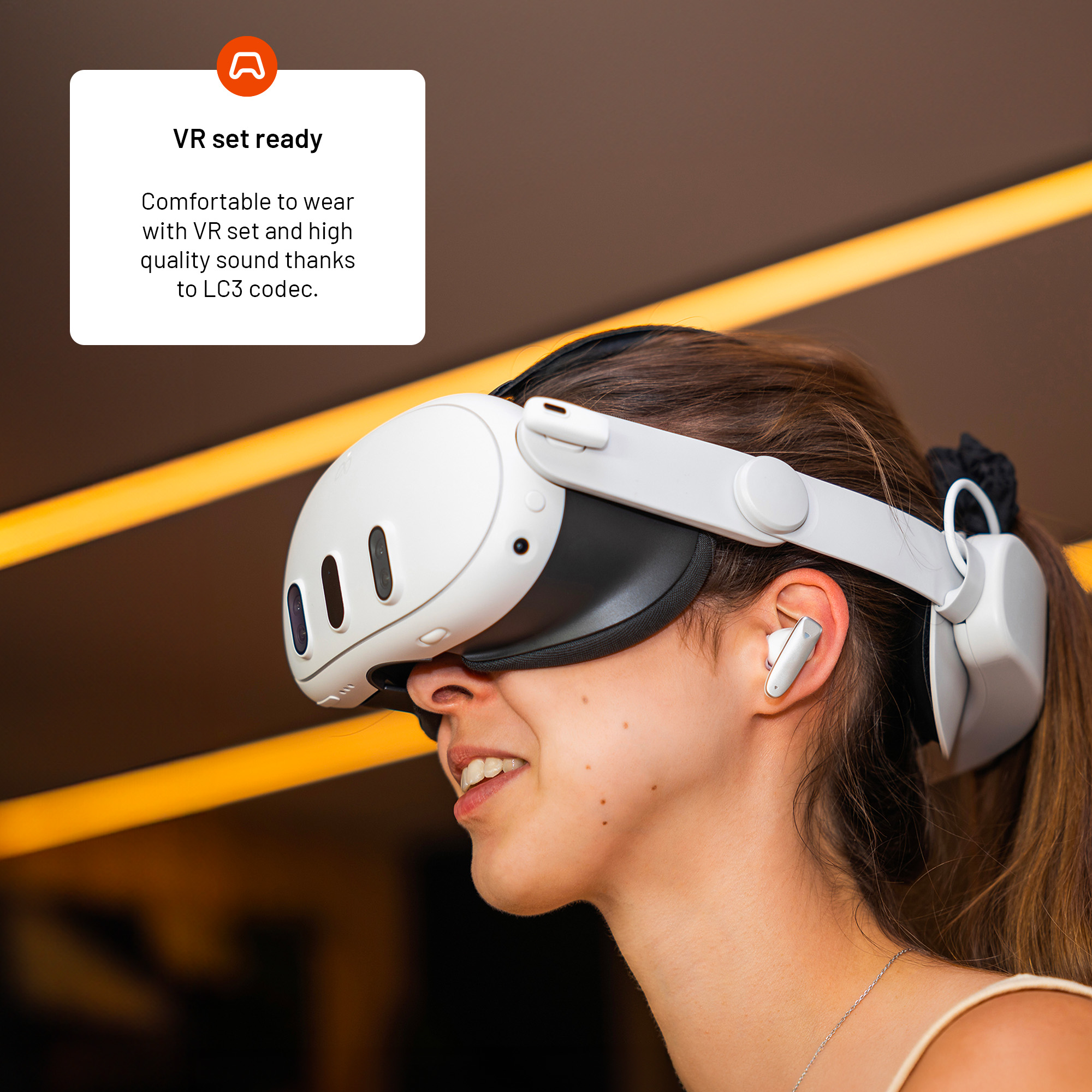 Eine Frau mit weißem VR-Headset und Ohrhörern lächelt. Der Hintergrund ist braun mit gelben Streifen.